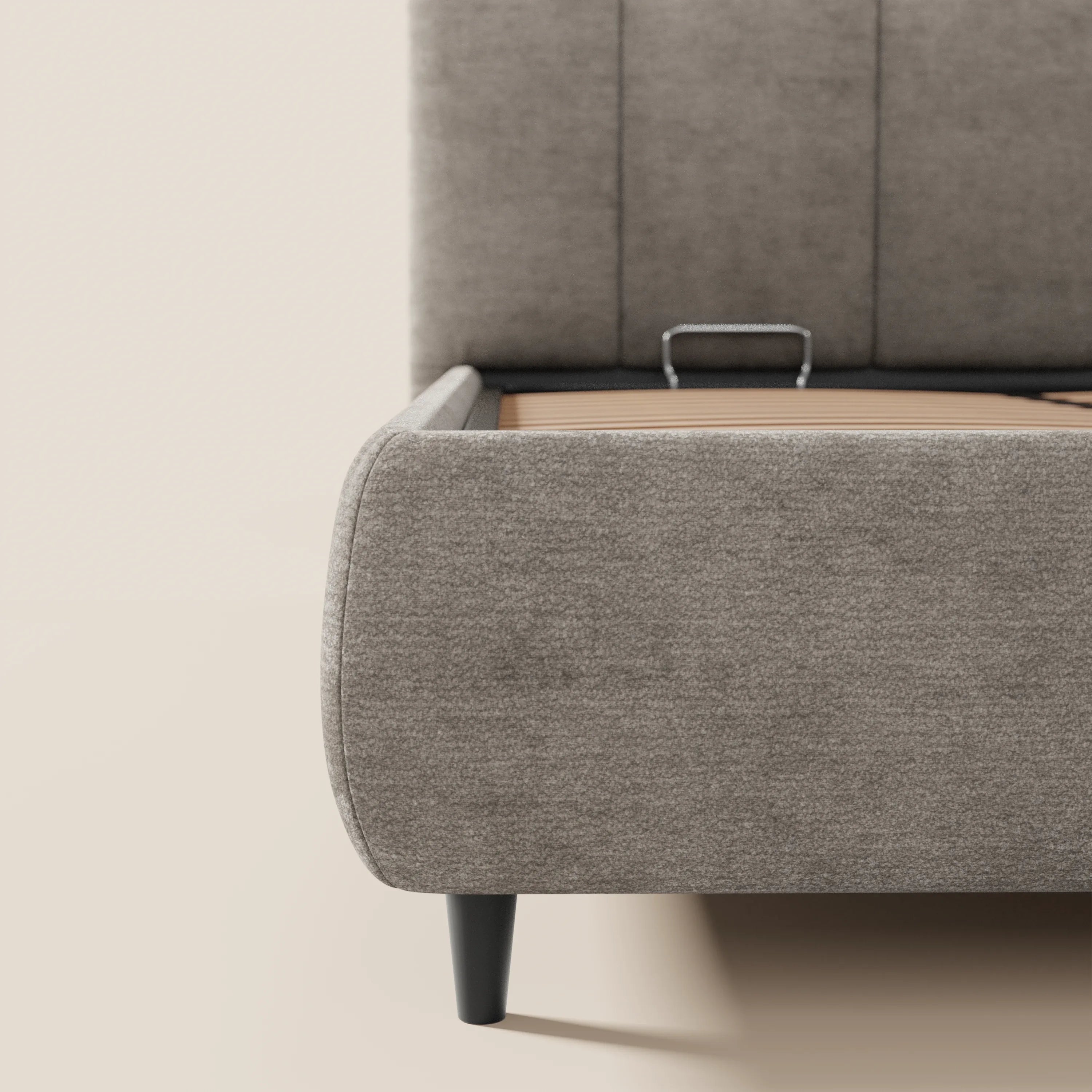 Primo piano del letto imbottito ARKAM di Letti.store, caratterizzato da un morbido tessuto grigio certificato Oeko-Tex®, pediera arrotondata, gambe corte nere e maniglia centrale in metallo: ideale per una camera da letto in stile shabby chic con soluzioni di contenimento intelligenti.