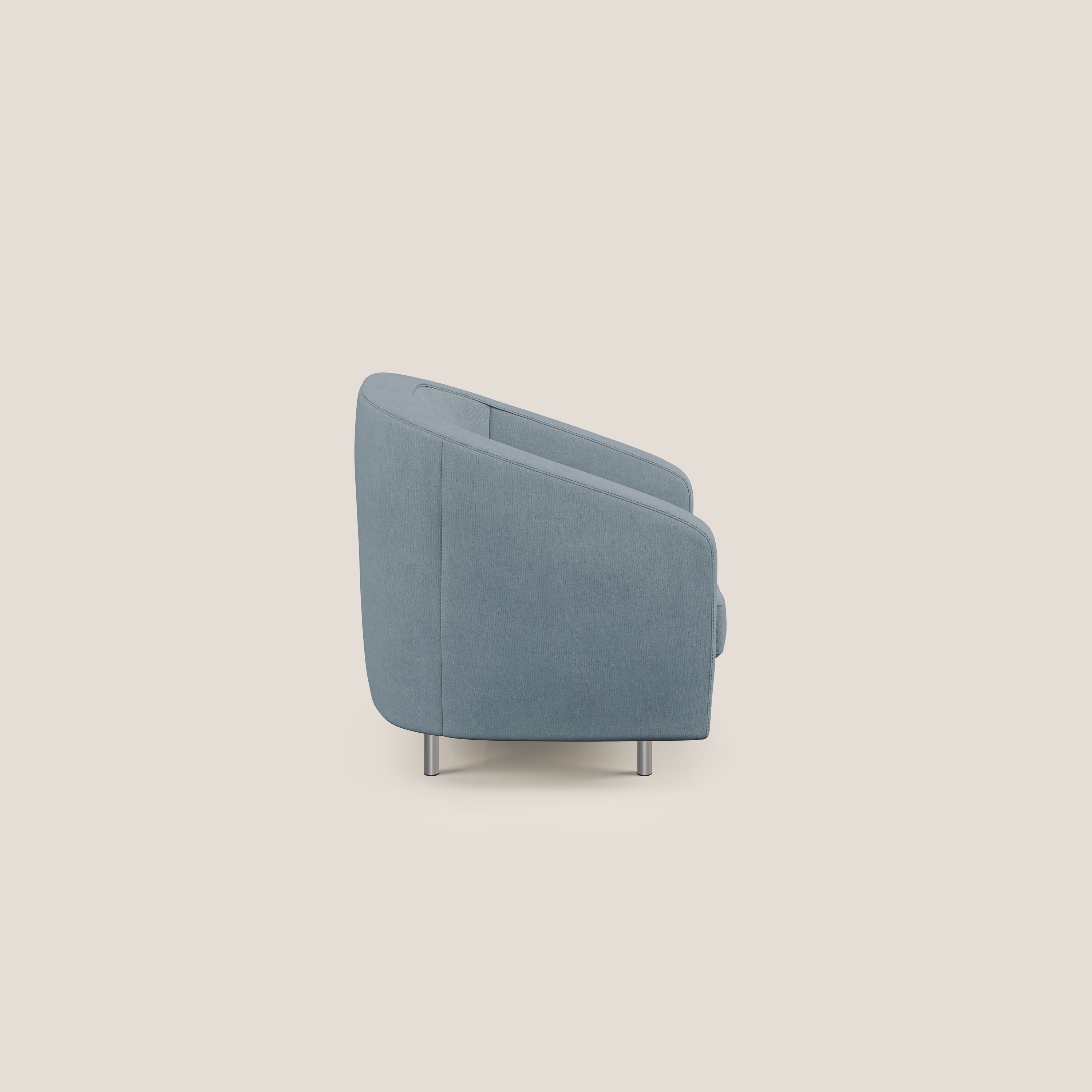 La poltroncina Sally in tessuto morbido impermeabile T02 carta da zucchero di Divani.Store si presenta lateralmente con linee morbide, braccioli e schienale dolcemente curvati e due gambe cilindriche in metallo su sfondo beige.