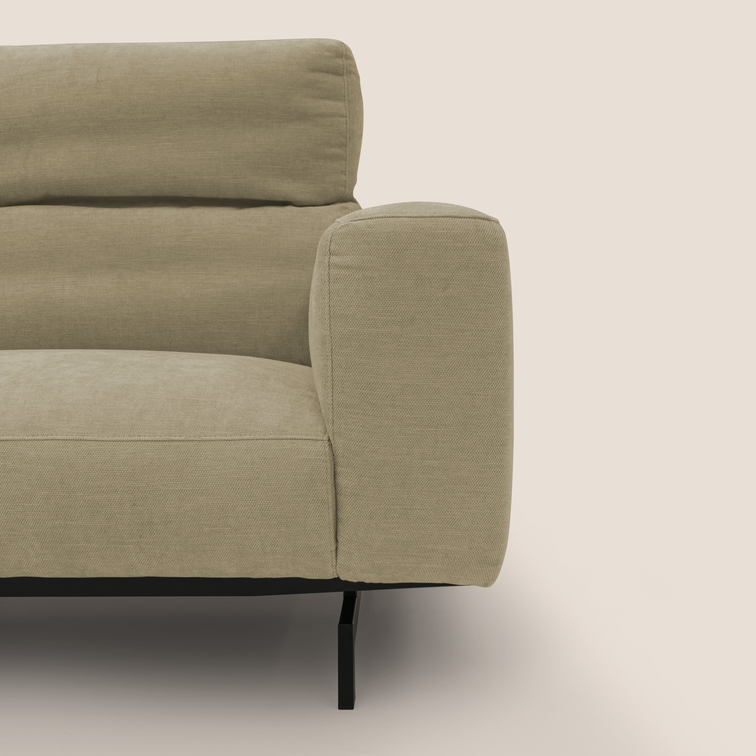Un primo piano del divano Sakura in piuma d'oca di Divani.Store, realizzato in morbido tessuto impermeabile T14 beige, mostra il bracciolo sinistro, la seduta e lo schienale dalle linee pulite, il ciuffo orizzontale e le sottili gambe in metallo nero su uno sfondo bianco sporco.