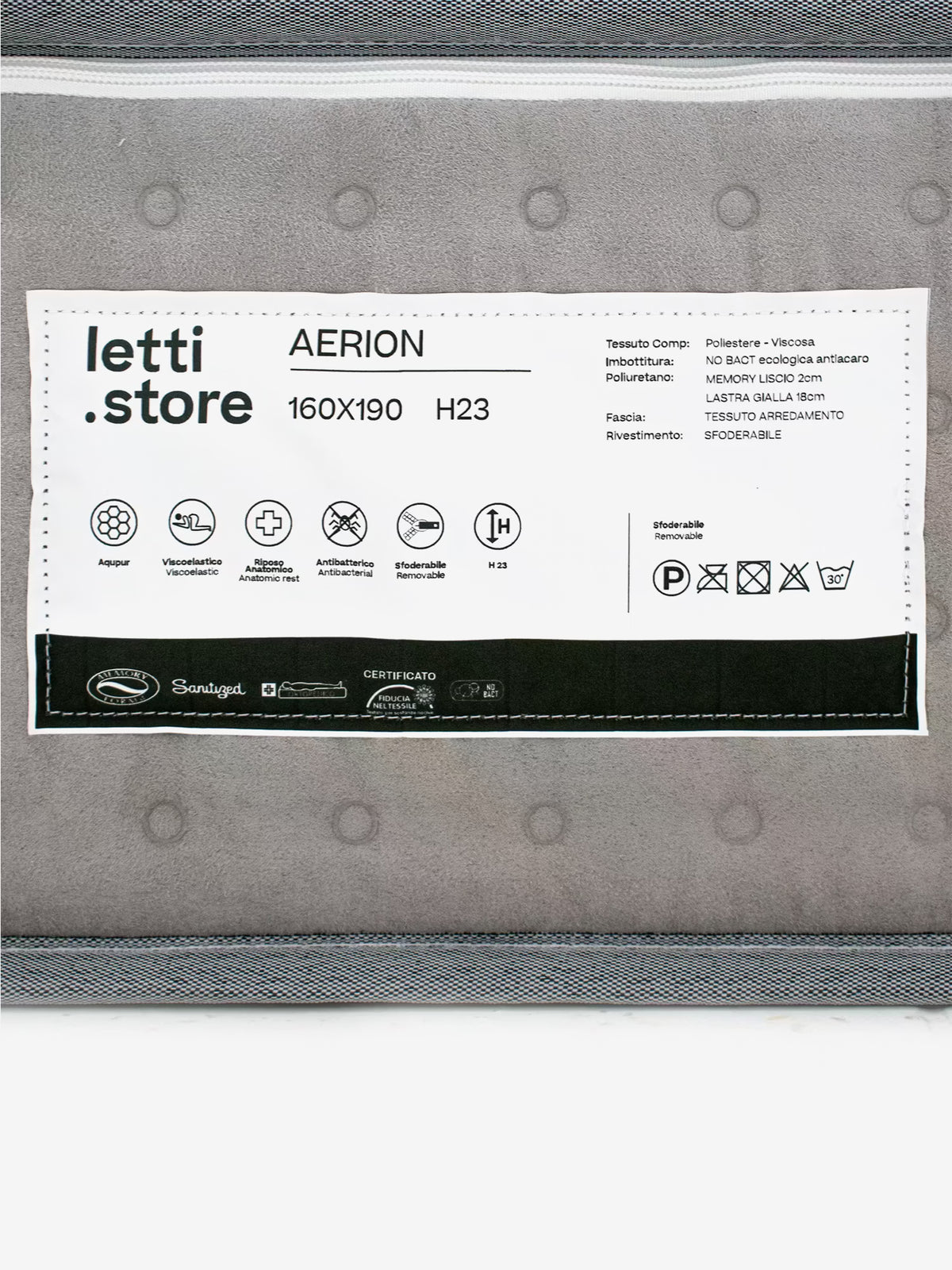 Primo piano dell’etichetta di un materasso su cui figurano il marchio “Divani.Store”, il nome del prodotto “AERION – Materasso ortopedico in Memory & Aquapur per un riposo leggero come l’aria”, le dimensioni 160x190 cm e l’altezza di 23 cm. L’etichetta riporta i dettagli sui materiali del tessuto ed evidenzia caratteristiche quali la schiuma memory, le proprietà antiacaro e antibatteriche, oltre ai simboli relativi alla manutenzione. Sullo sfondo è visibile il motivo a cuciture del tessuto del materasso.