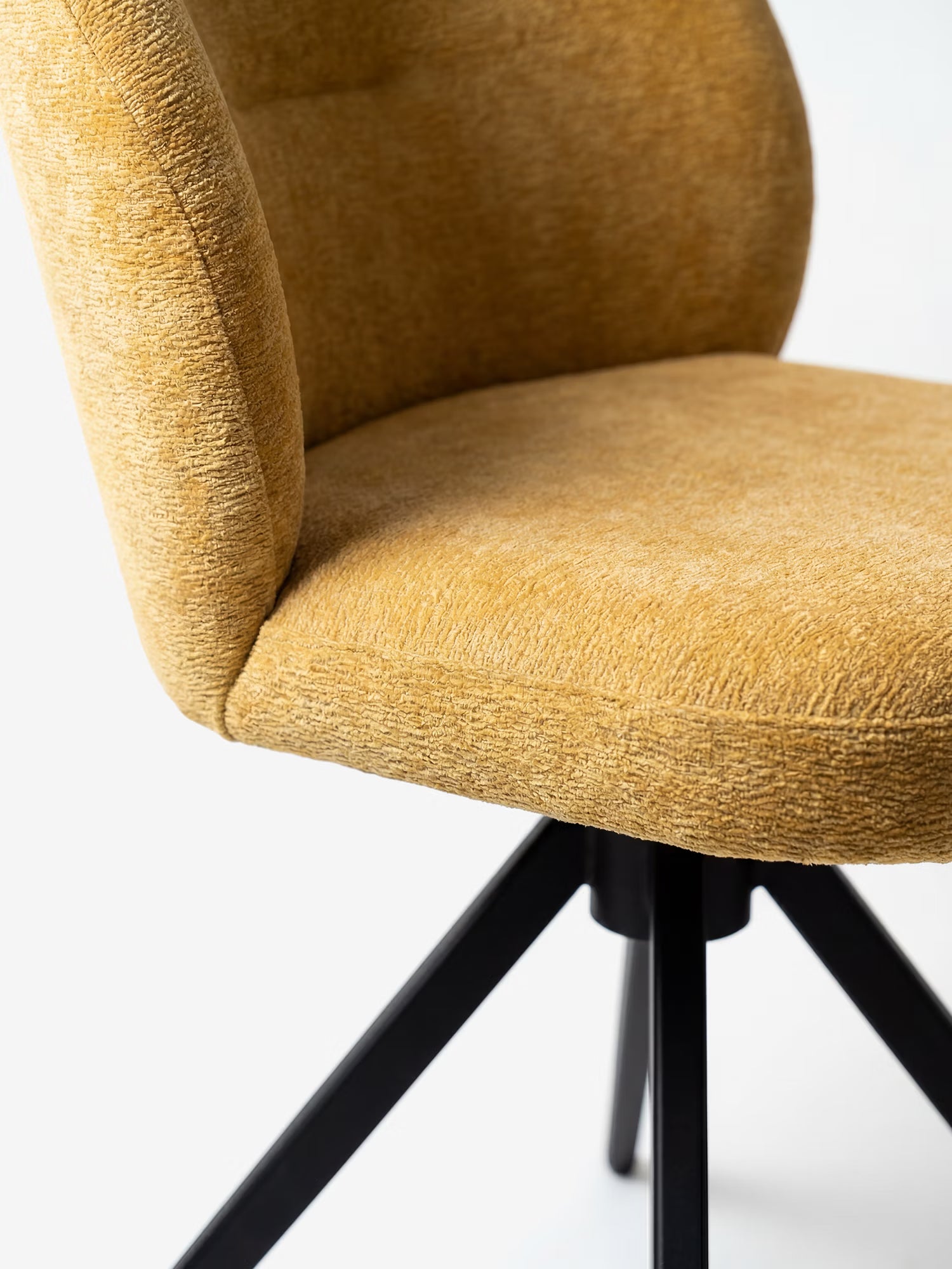 Primo piano della sedia imbottita Alba di Divani.Store, realizzata in tessuto effetto cotone color giallo senape certificato OEKO-TEX®, con seduta imbottita, schienale ricurvo e base in metallo nero su uno sfondo bianco a tinta unita.