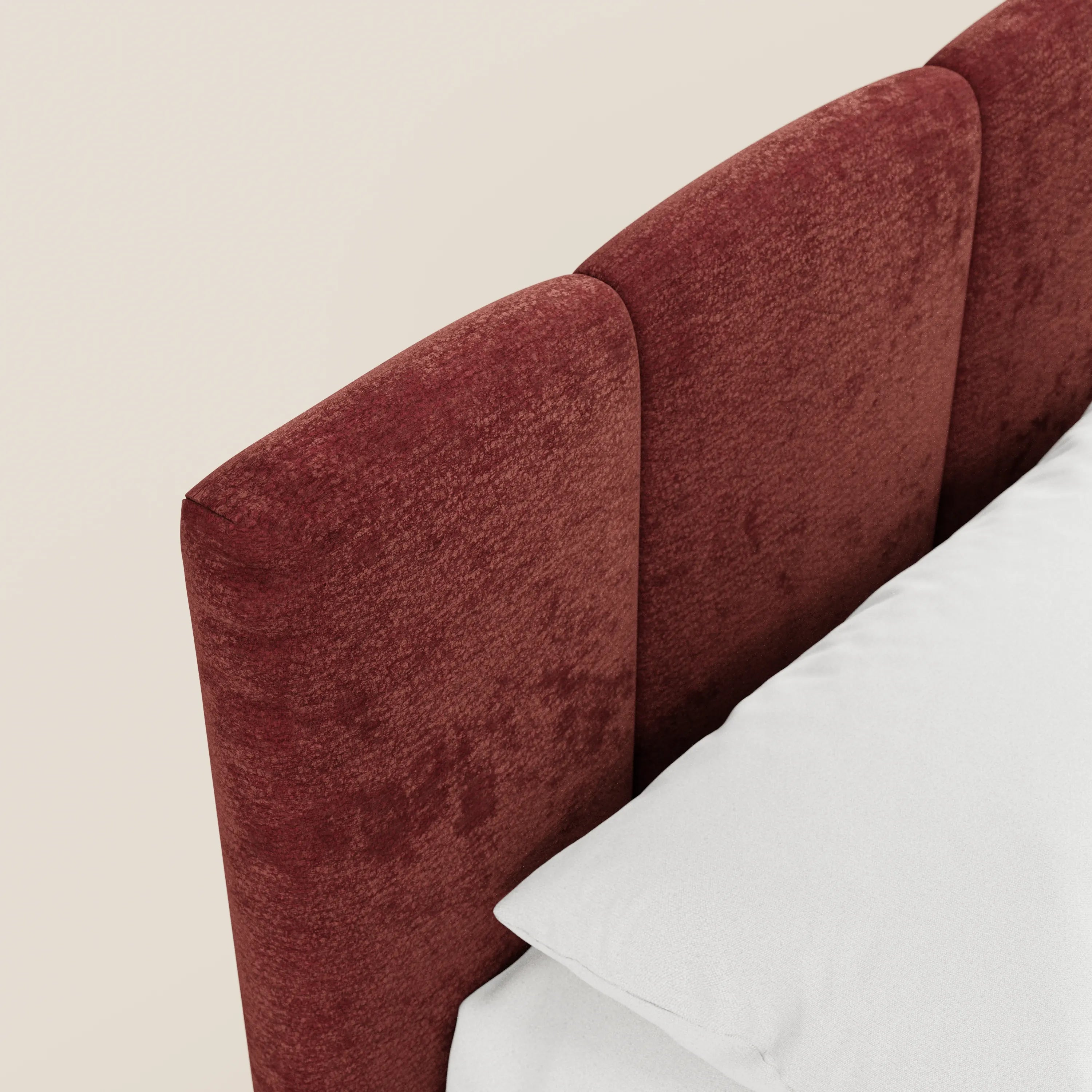Un primo piano del letto imbottito ARKAM di Letti.store mette in risalto il suo tessuto rosso scuro, certificato Oeko-Tex®, e la testiera in stile shabby chic con pannelli verticali, abbinata a biancheria da letto bianca su uno sfondo beige chiaro.