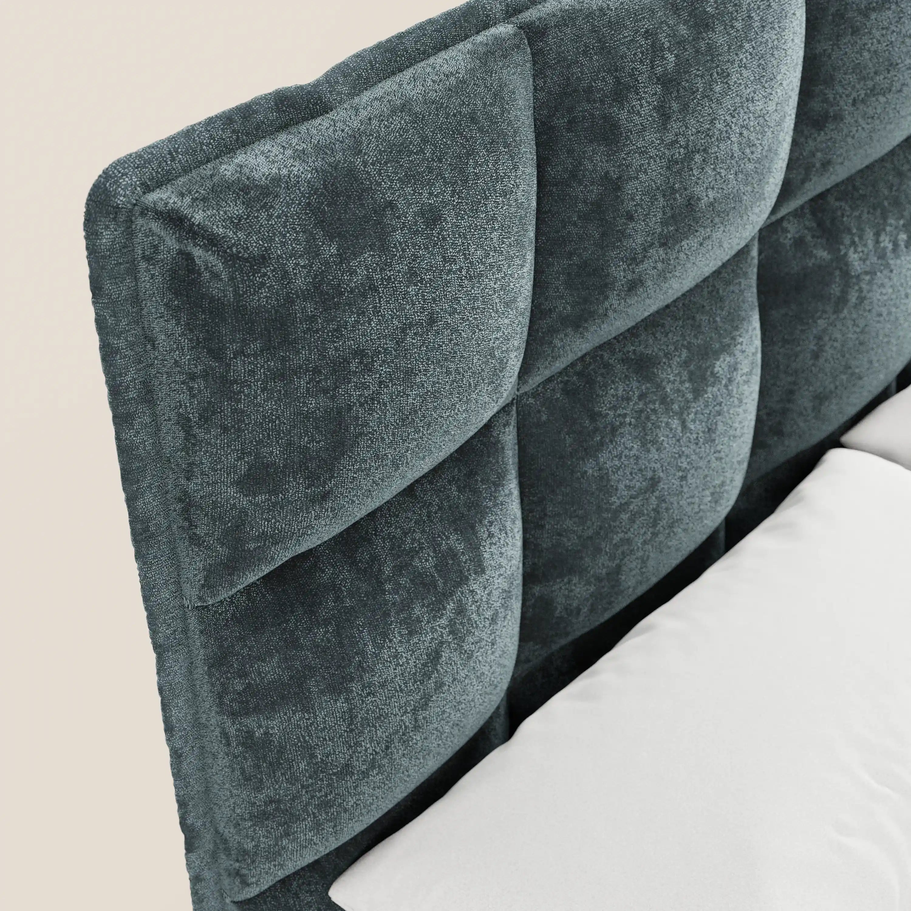 Primo piano del letto imbottito AURO di Letti.store, caratterizzato da una testiera in ciniglia color verde acqua scuro certificata Oeko-Tex® con morbida trapuntatura capitonné a quadrati e base contenitiva, raffigurato con un cuscino bianco e un materasso su uno sfondo beige chiaro.