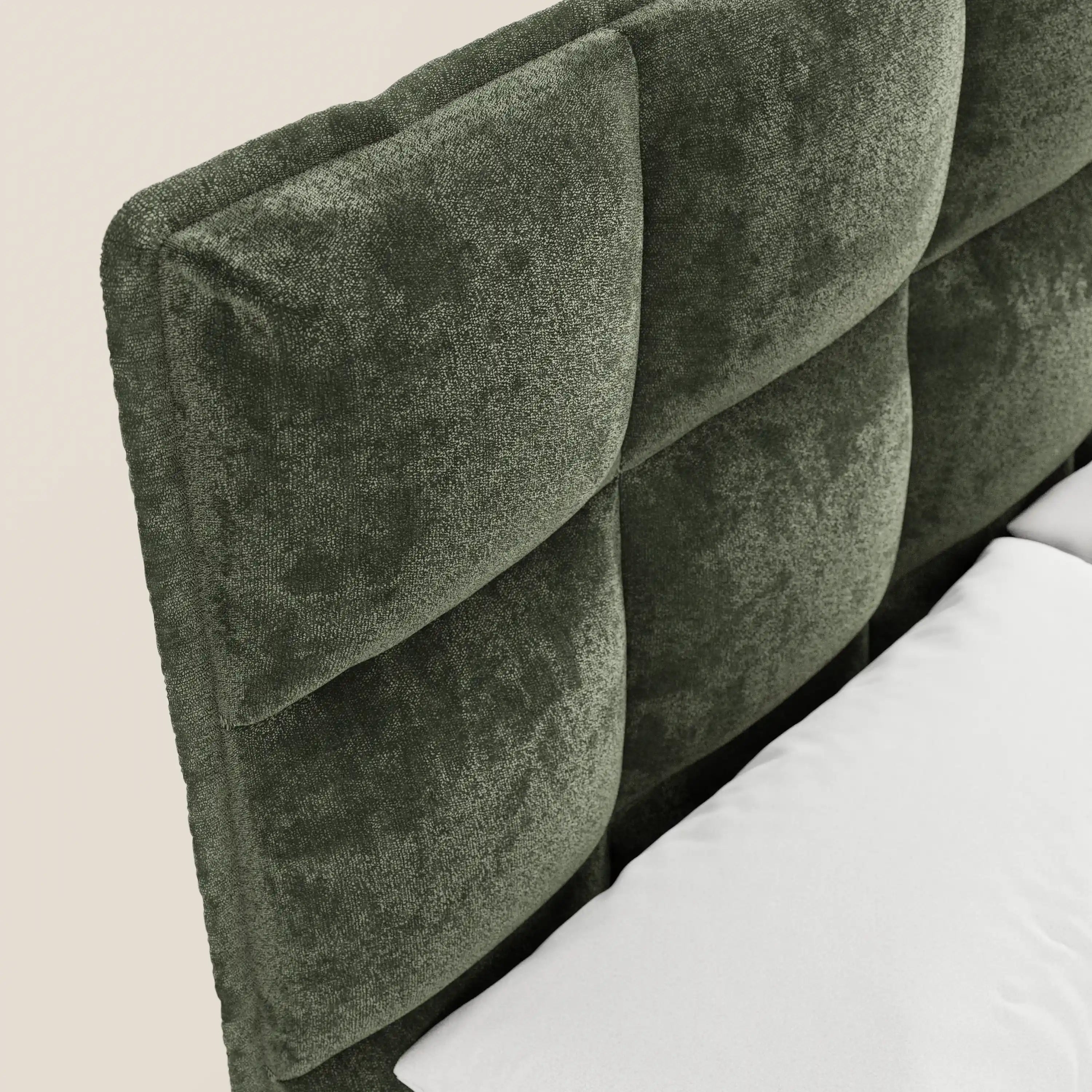 Primo piano del letto imbottito AURO di Letti.store, caratterizzato da un’alta e morbida testiera capitonné in ciniglia verde scuro certificata Oeko-Tex®. La testiera, dalla trama rigata, presenta grandi bottoni quadrati, con un cuscino bianco appoggiato contro questo letto dal design moderno.