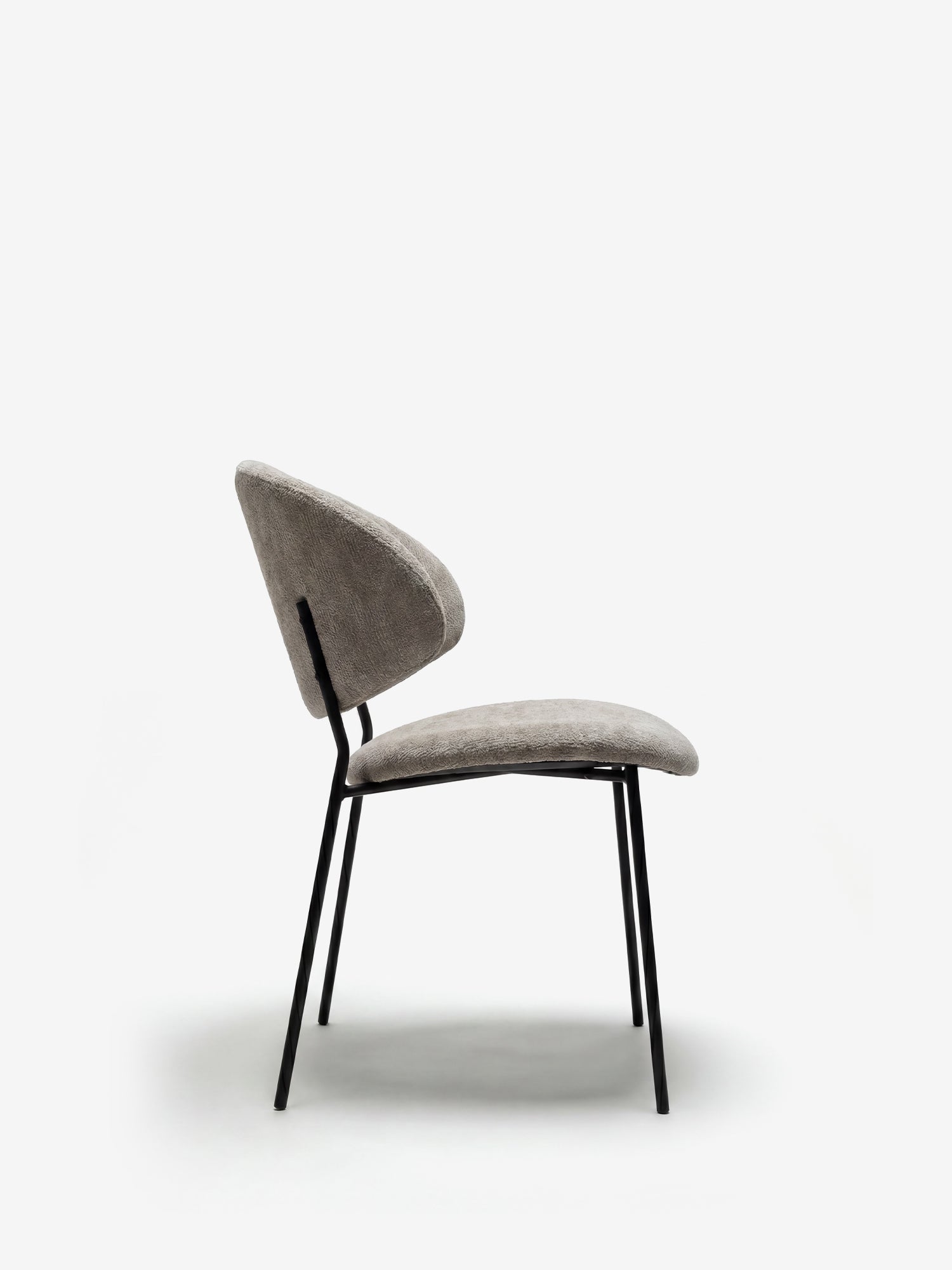 La sedia Bruma di Divani.Store è caratterizzata da un elegante tessuto goffrato in grigio chiaro, uno schienale avvolgente e sottili gambe in metallo nero, che ne esaltano il design minimalista su uno sfondo bianco a tinta unita.