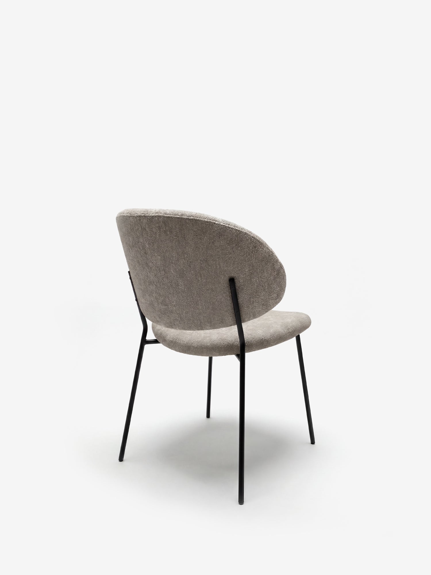 La sedia Bruma di Divani.Store, con uno schienale avvolgente in elegante tessuto goffrato grigio chiaro e sottili gambe in metallo nero, è raffigurata su sfondo bianco da un'angolazione posteriore a tre quarti. Design minimalista e contemporaneo.