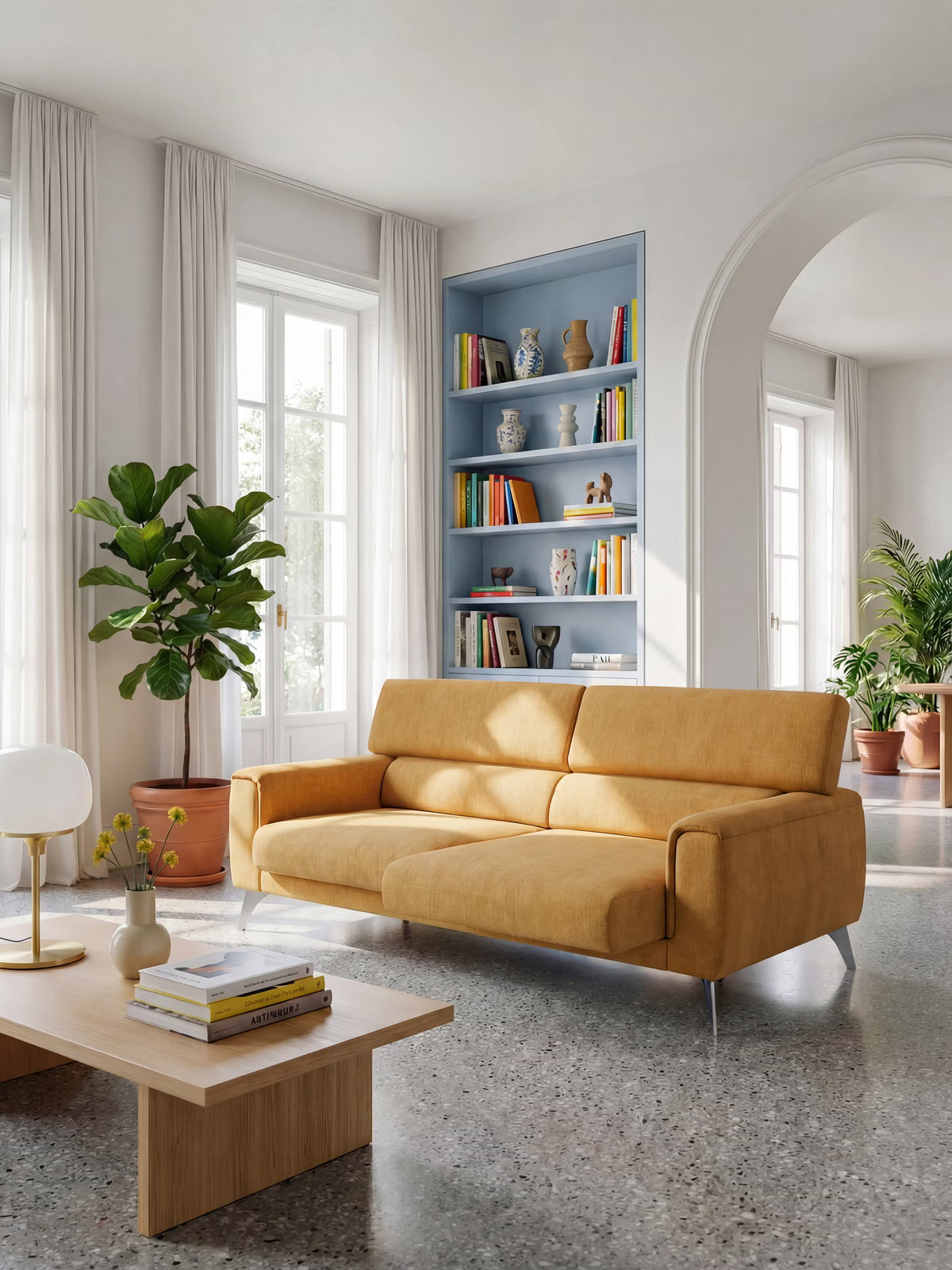 Un soggiorno moderno arredato con il divano Caravaggio a 2 e 3 posti, dotato di sedute allungabili e poggiatesta reclinabili, rivestito nell’elegante tessuto smacchiabile T31 di Divani.Store in un vivace giallo senape. Lo spazio comprende un tavolino basso in legno, una grande pianta in vaso, una libreria a muro blu adornata con libri e oggetti decorativi, pareti bianche, una porta ad arco, pavimento in terrazzo e finestre alte con tende trasparenti. Il design versatile del divano Caravaggio offre un