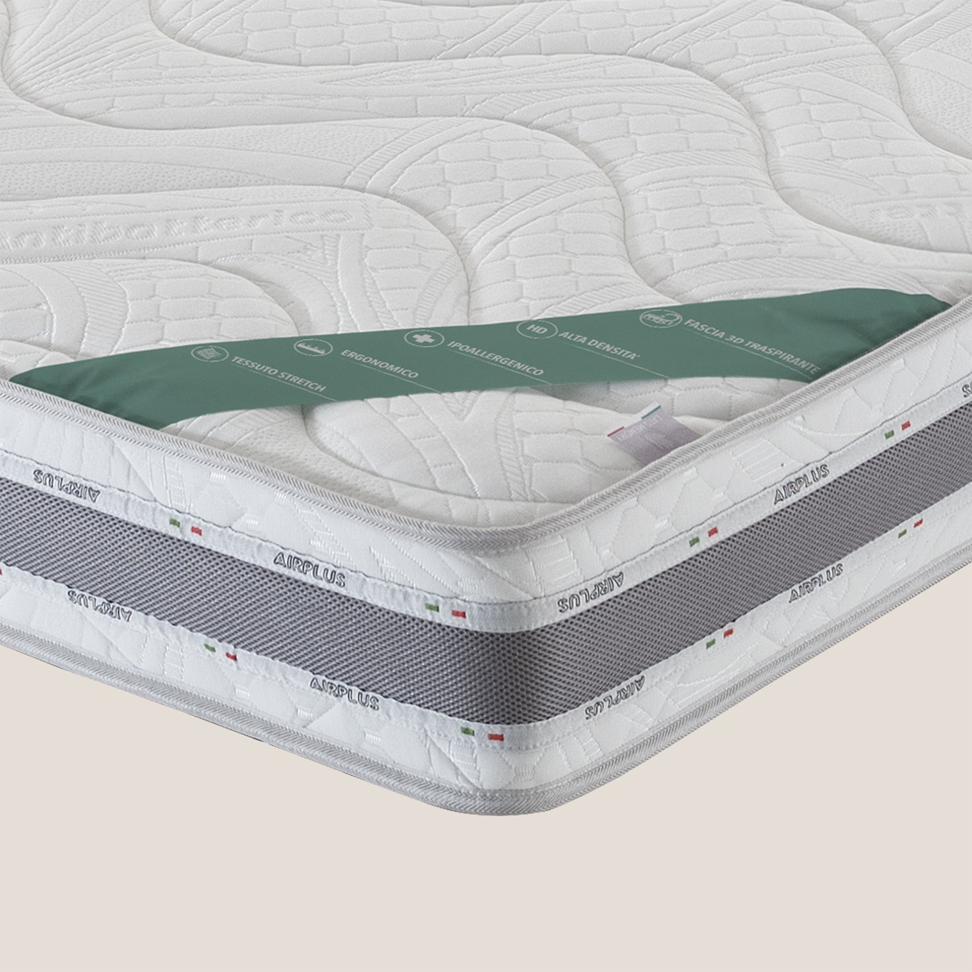 Un primo piano del materasso in memory foam Comfort+ H18 cm di Divani.Store mostra l'angolo bianco trapuntato con accento verde, la scritta "antibacterial", la rete traspirante grigia in tessuto anallergico, le etichette ARTPLUS e bandiera italiana. Le etichette sono parzialmente visibili.