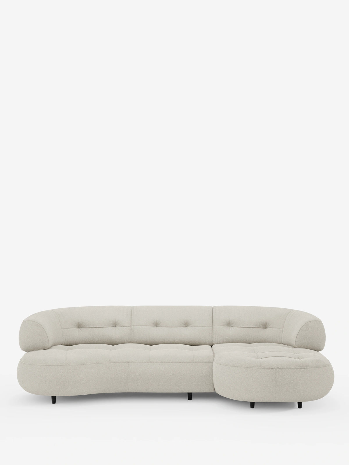 Un divano angolare Croissant color beige, dal design a forma di fagiolo e con schienali scorrevoli, rivestito in morbido tessuto effetto cotone smacchiabile T33, caratterizzato da bordi arrotondati, cuscini trapuntati e piccole gambe scure su sfondo bianco.