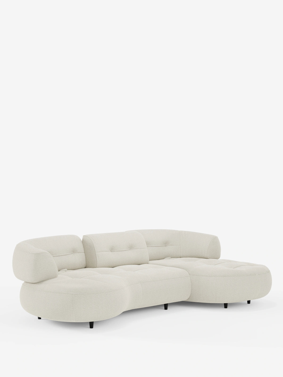 Un divano angolare Croissant beige a forma di fagiolo, con schienali scorrevoli in morbido tessuto effetto cotone lavabile, modello T33: divano componibile con bordi arrotondati, schienali trapuntati con bottoni e gambe corte nere su fondo bianco.