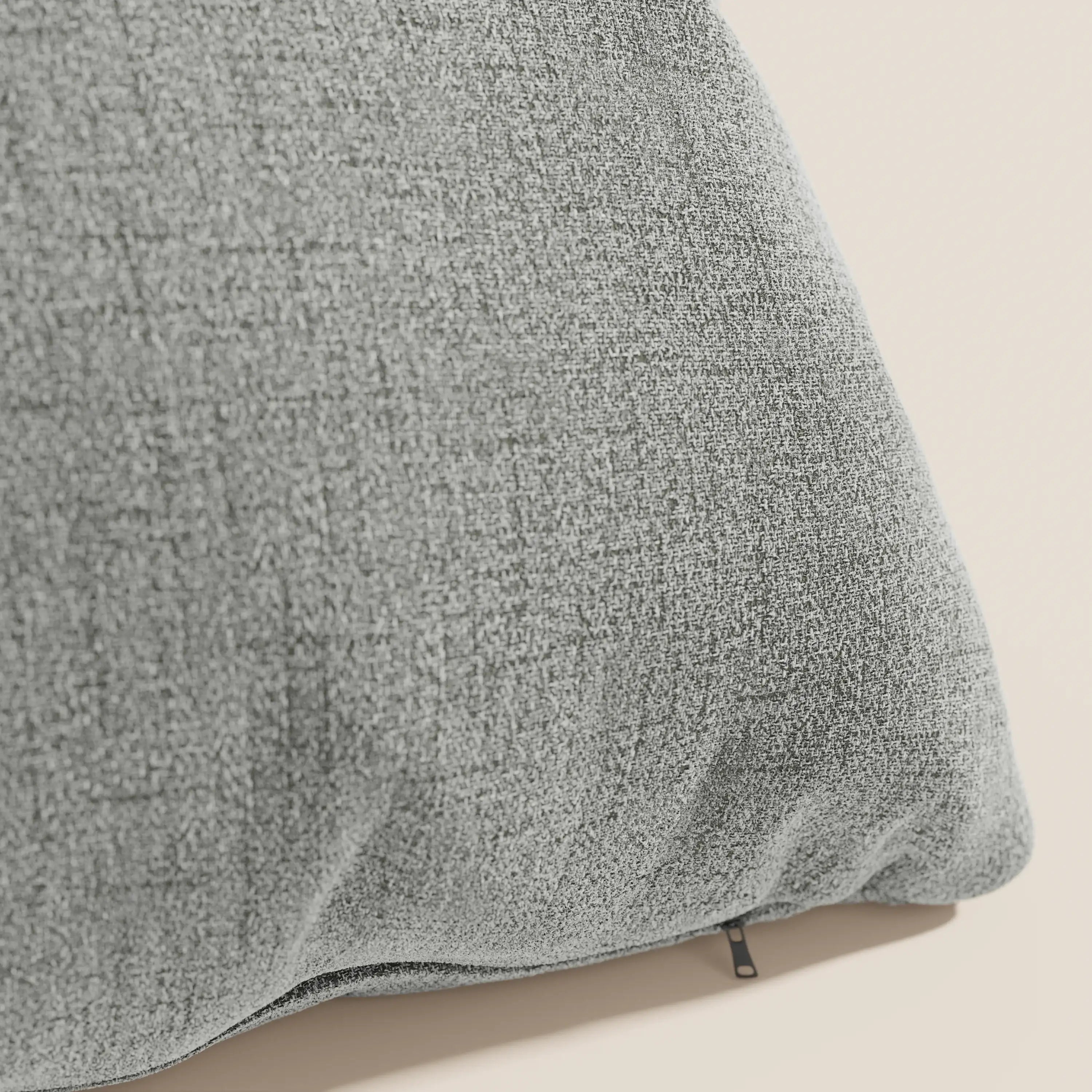 Primo piano del cuscino Felis di Divani.Store in T03 grigio chiaro, realizzato in morbido tessuto idrorepellente, caratterizzato da una piccola cerniera nera sul bordo inferiore su uno sfondo beige chiaro.