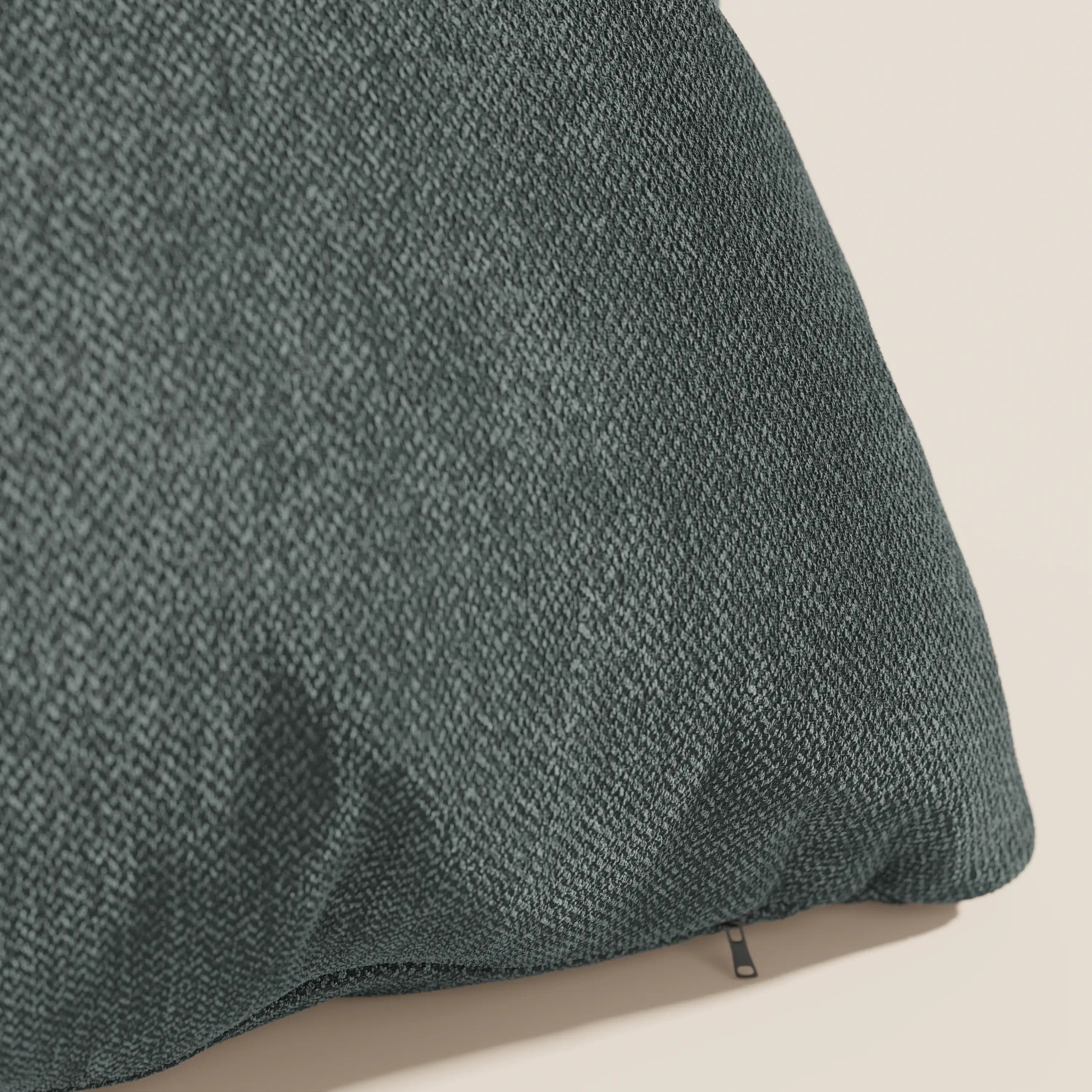 Primo piano del cuscino Sogno cuscino di Divani.Store in SMACCHIABILE T05 verde: un cuscino verde scuro, dalla texture morbida, con un sottile disegno a spina di pesce e una discreta cerniera, mostrato su uno sfondo beige chiaro. Disponibile in vari colori.