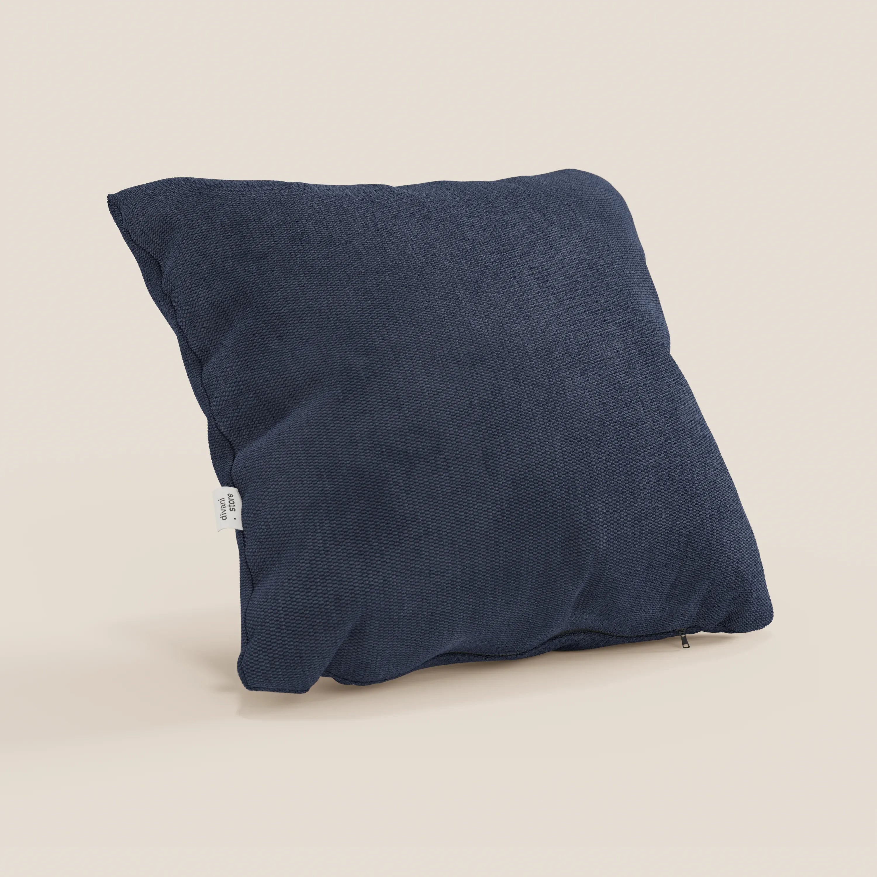 Il cuscino Miami di Divani.Store, in tessuto impermeabile T14 blu e forma quadrata, è mostrato in piedi contro uno sfondo beige chiaro; presenta una trama leggermente ruvida, zip visibile sul bordo inferiore e piccolo tag bianco laterale.