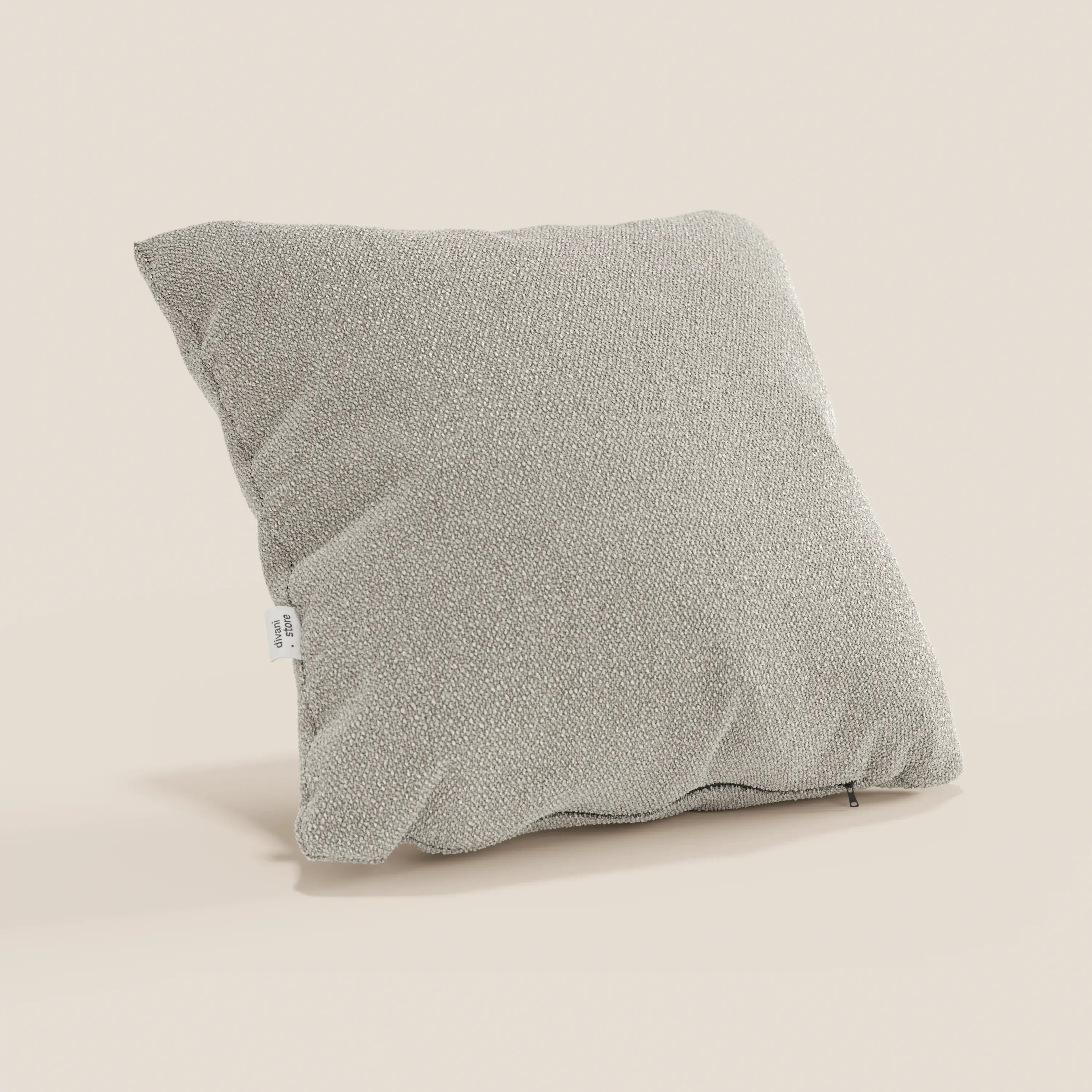 Un cuscino Lambada grigio chiaro di Divani.Store in tessuto smacchiabile e impermeabile tipo cotone naturale si erge su uno sfondo beige. Su un lato è presente una piccola etichetta bianca e sul bordo inferiore è visibile una cerniera nera.