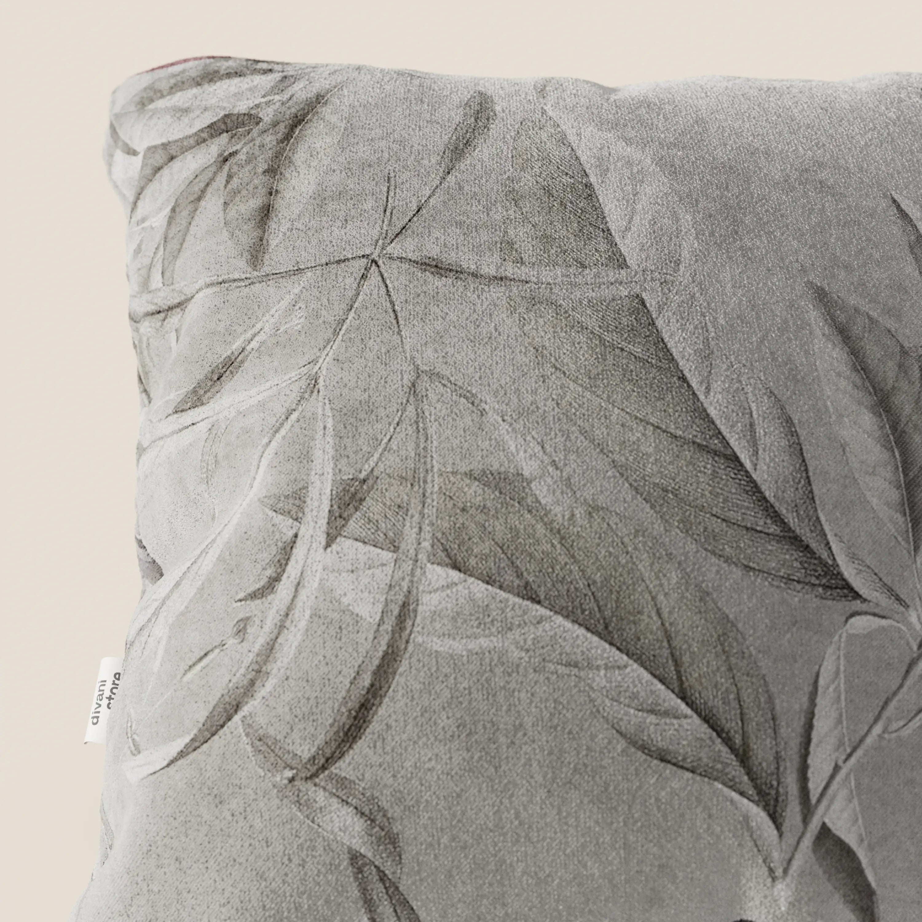 Un primo piano della collezione Lemon elegante di cuscini a fantasia in velluto impermeabile grigio di Divani.Store mostra un motivo a foglie in rilievo, un'etichetta laterale bianca e un'elegante texture su uno sfondo beige chiaro.