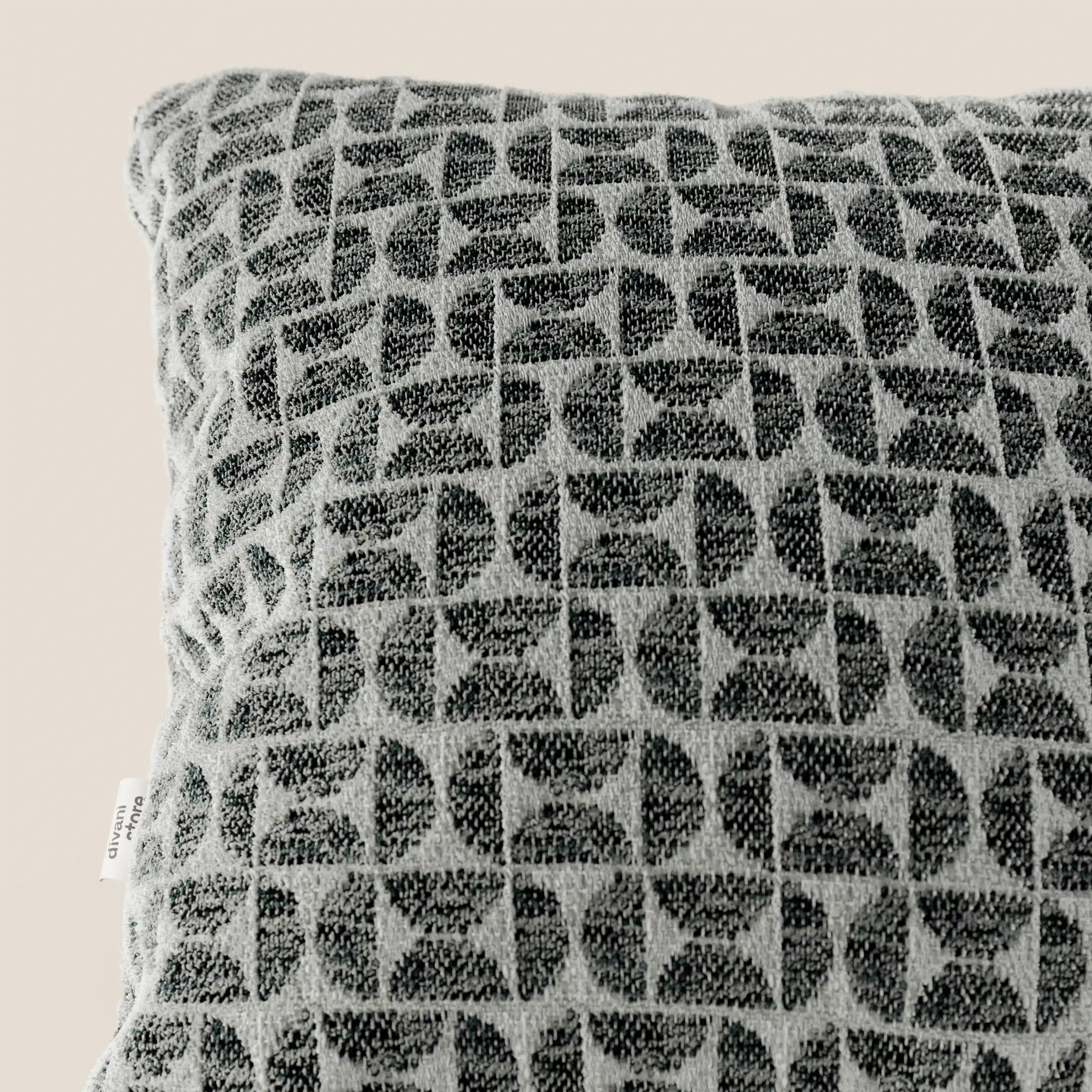 Primo piano del cuscino Naxos Cuscino Decoro 45x45 in Lino di Divani.Store, un cuscino quadrato grigio con un elegante motivo geometrico ad archi e un tessuto morbido e ruvido al tatto. Su uno sfondo beige a tinta unita è visibile una piccola etichetta bianca.
