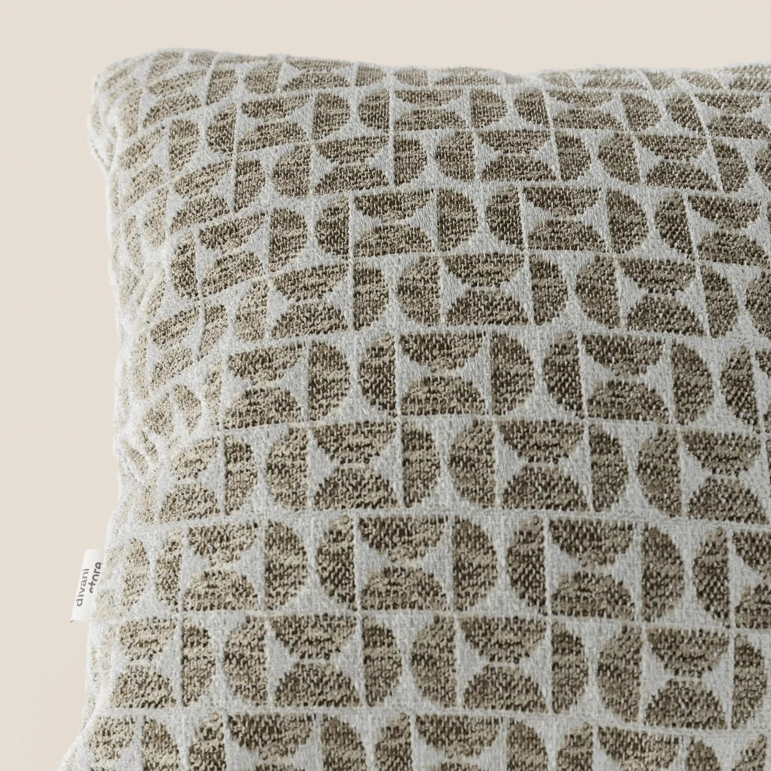 Un primo piano del modello Naxos Cuscino Decoro 45x45 in Lino di Divani.Store ne mette in risalto l'elegante motivo geometrico a griglia nei toni del marrone e del beige, il tessuto in lino intrecciato dalla trama ruvida e l'etichetta bianca sul bordo sinistro, il tutto su uno sfondo neutro e delicato.