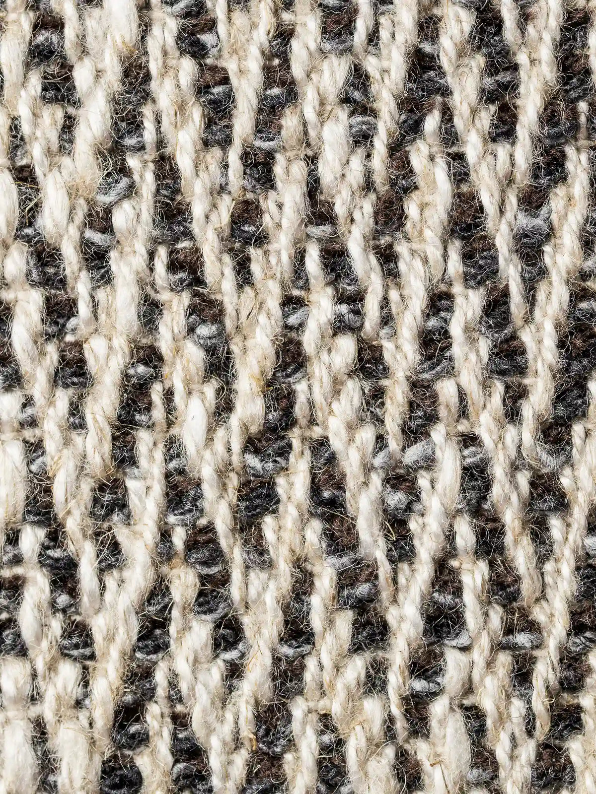 Primo piano su S04 CHEVRON esclusivo, tessuto naturale in viscosa, lino e cotone, caratterizzato da un motivo a zigzag in rilievo nei toni del crema, marrone scuro e grigio, con fili spessi e intrecciati che conferiscono alla superficie una consistenza densa e piacevole al tatto.