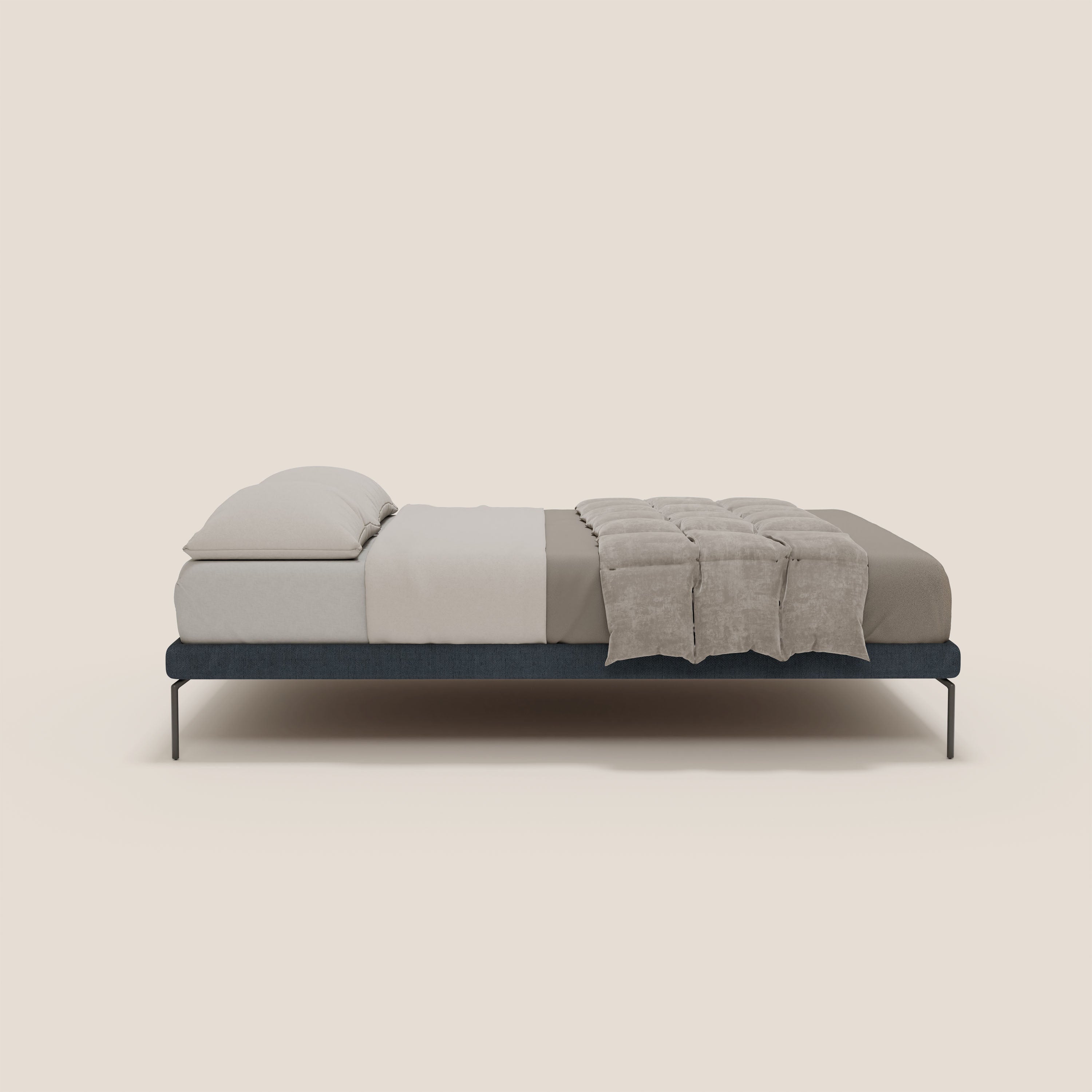 Il sommier sfoderabile Ring di Letti.store è caratterizzato da gambe alte 24 cm e da un tessuto impermeabile blu T14, vestito con lenzuola beige chiaro, due cuscini e una coperta trapuntata tortora: un design italiano minimalista su uno sfondo crema.