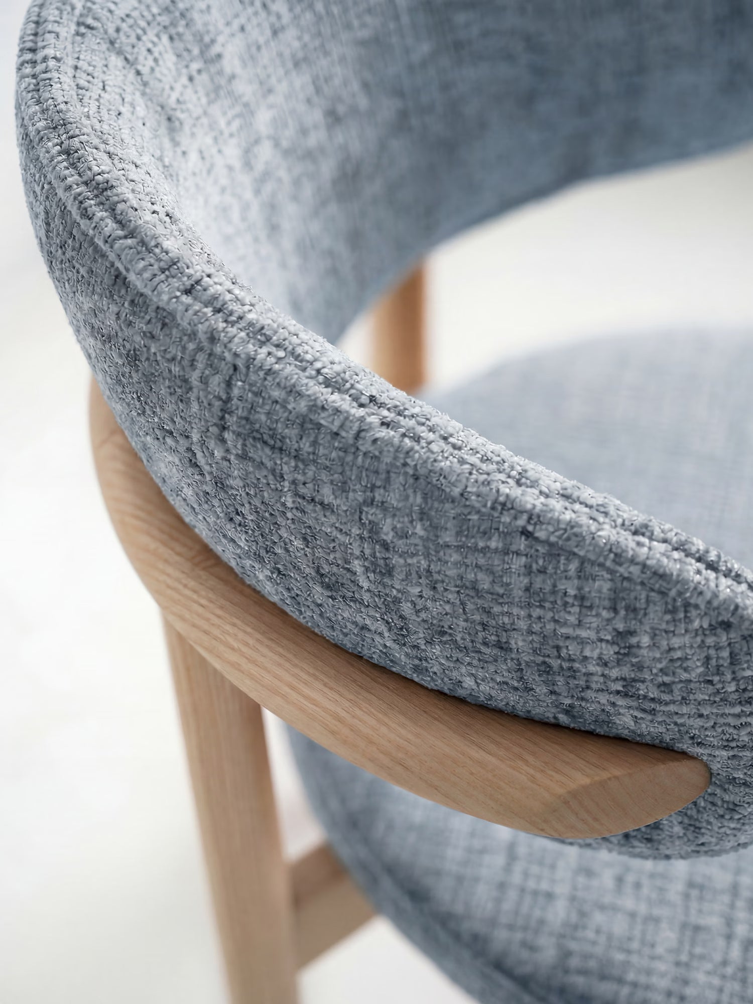 Primo piano della sedia imbottita Dafne di Divani.Store, realizzata in rovere massello naturale con tessuto chenille certificato OEKO-TEX®. Presenta uno schienale imbottito e curvo e un design minimalista che unisce la morbidezza del tessuto all’eleganza del legno.