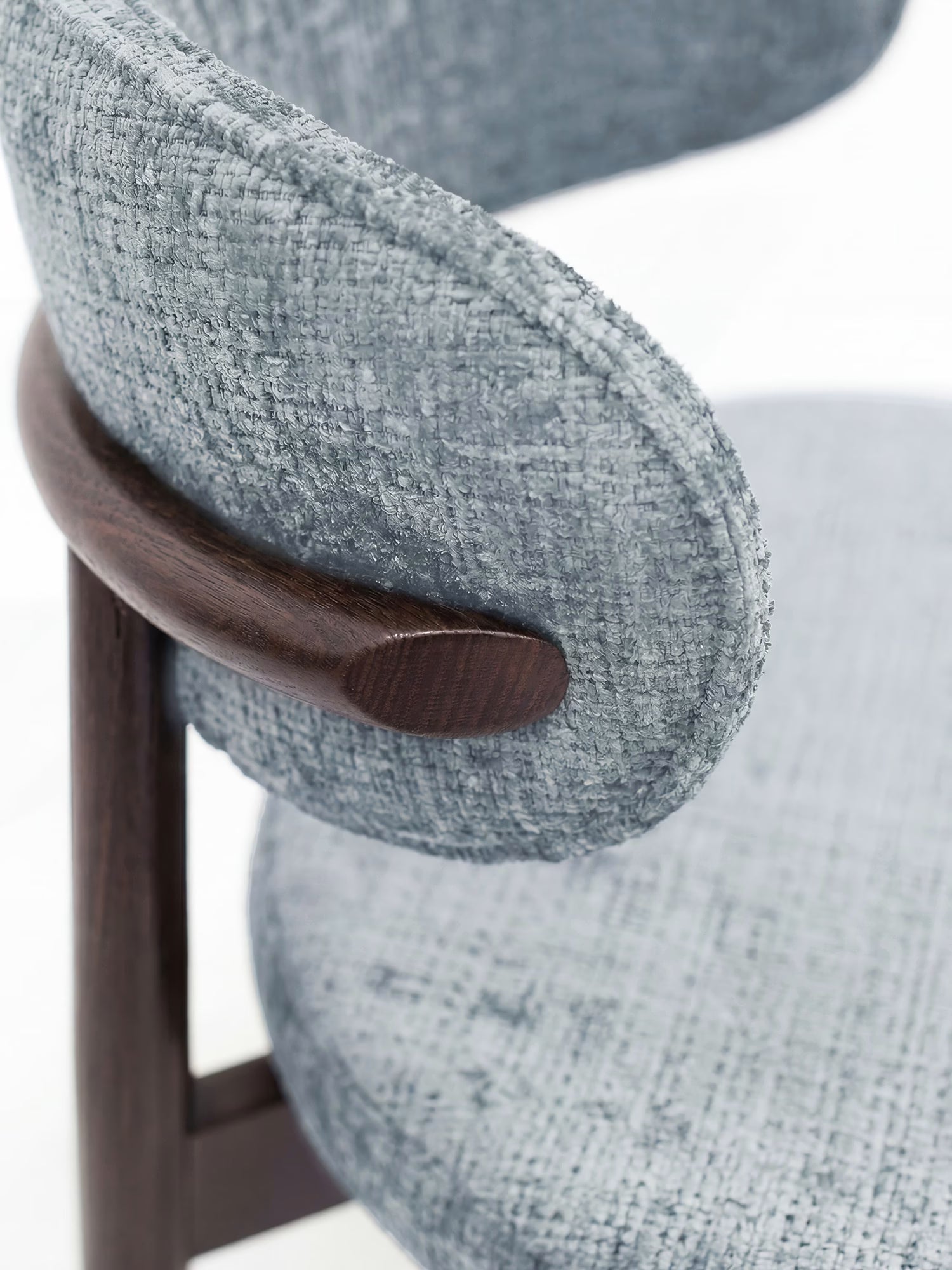 Primo piano della sedia imbottita Dafne di Divani.Store, realizzata in tessuto ciniglia grigio chiaro certificato OEKO-TEX® e caratterizzata da uno schienale arrotondato che si fonde con le gambe in legno massello di wengé, mettendo in risalto il contrasto tra il morbido rivestimento e la levigatezza del legno.