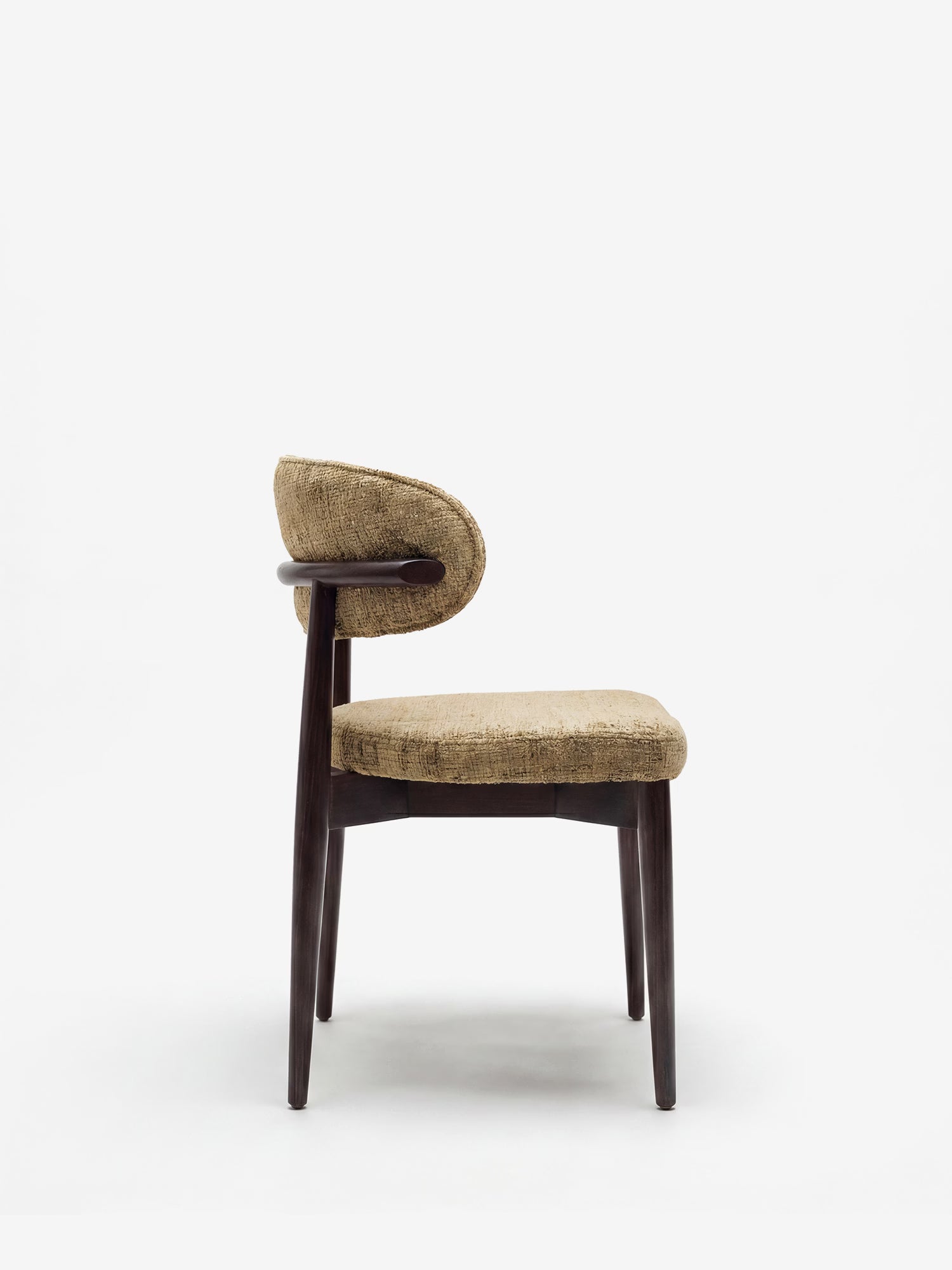 La vista laterale della sedia di design imbottita “Dafne” di Divani.Store presenta una struttura in legno massello di wengé con quattro gambe e un rivestimento in ciniglia certificato OEKO-TEX® in marrone chiaro testurizzato, che risalta sullo sfondo bianco a tinta unita, esaltandone l’elegante semplicità.