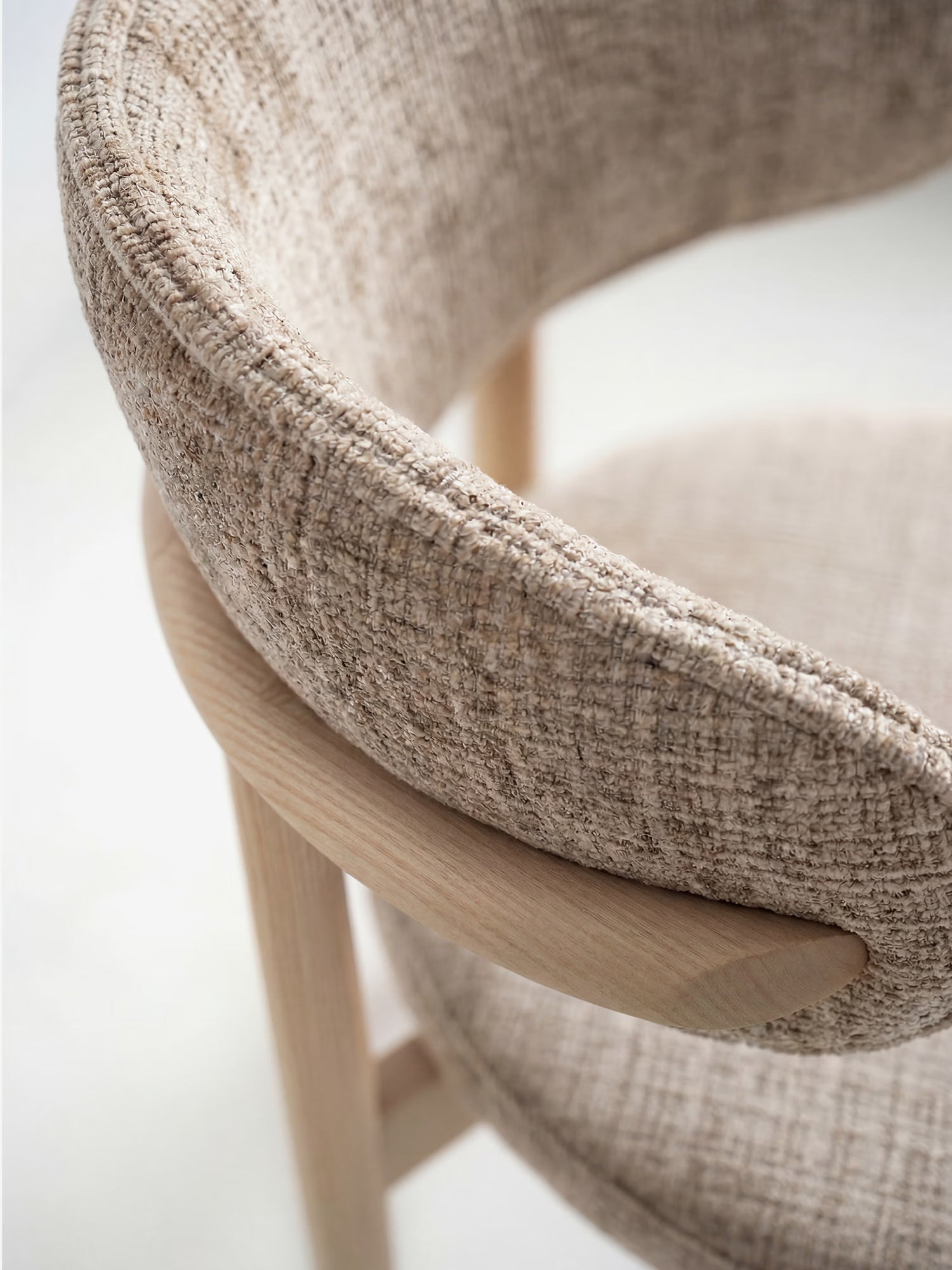 Primo piano della sedia imbottita Dafne di Divani.Store, caratterizzata da uno schienale curvo e imbottito e da un rivestimento in ciniglia OEKO-TEX® color beige, con gambe in rovere naturale massiccio che le conferiscono uno stile minimalista e contemporaneo.