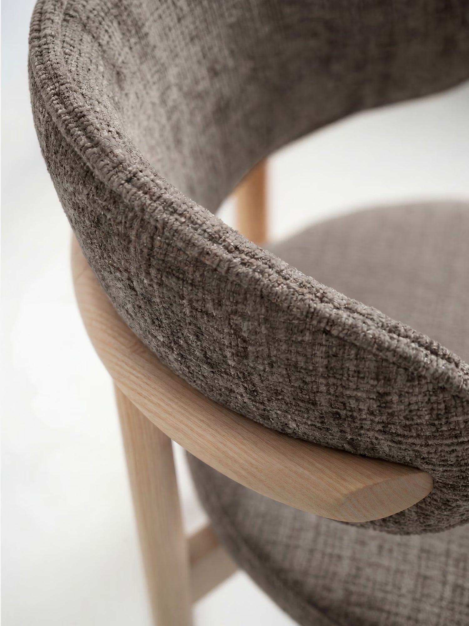 Primo piano della sedia imbottita Dafne di Divani.Store, caratterizzata da una morbida seduta in ciniglia certificata OEKO-TEX® nei toni del grigio-marrone e da uno schienale curvo con struttura a vista in rovere massello naturale.