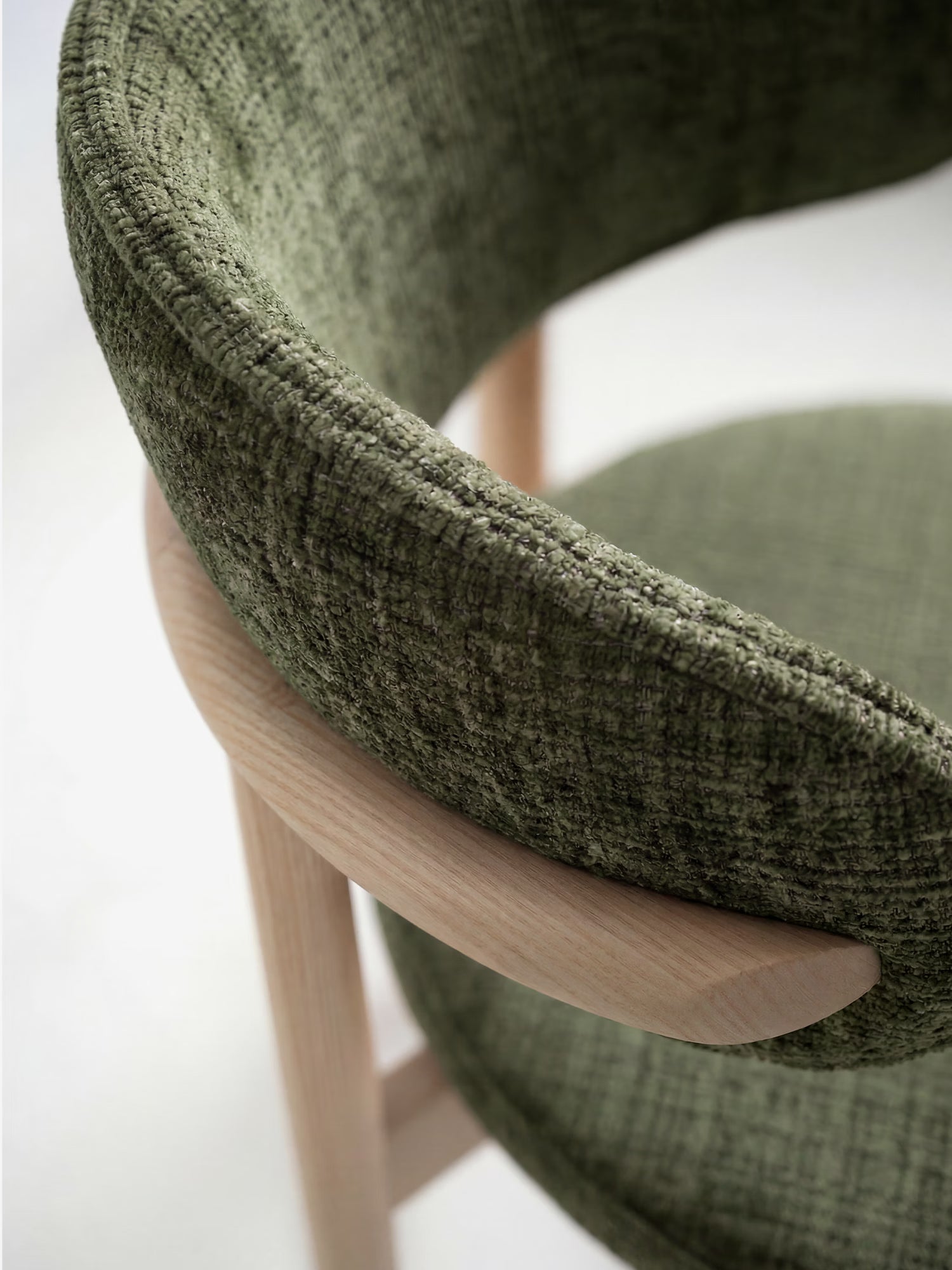 Primo piano della sedia imbottita Dafne di Divani.Store, realizzata in tessuto ciniglia verde oliva certificato OEKO-TEX® e caratterizzata da uno schienale curvo con gambe e braccioli in rovere massello naturale liscio, che creano un suggestivo contrasto tra legno e tessuto.