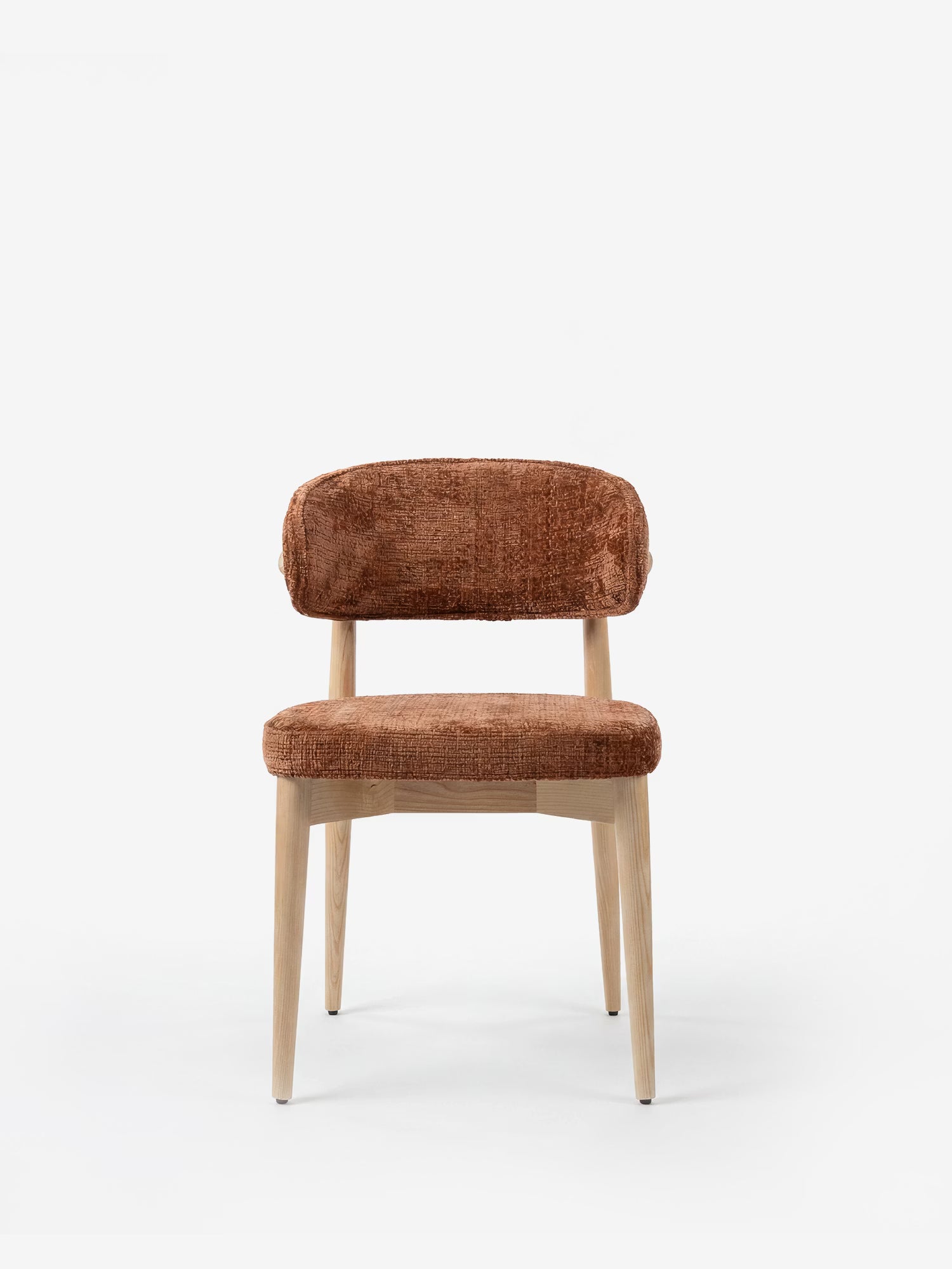 La sedia imbottita Dafne di Divani.Store presenta gambe in rovere naturale massiccio e una seduta ricurva, rivestita in morbida ciniglia marrone certificata OEKO-TEX®, che unisce il minimalismo moderno al comfort. Senza braccioli. Ripresa su uno sfondo bianco a tinta unita.