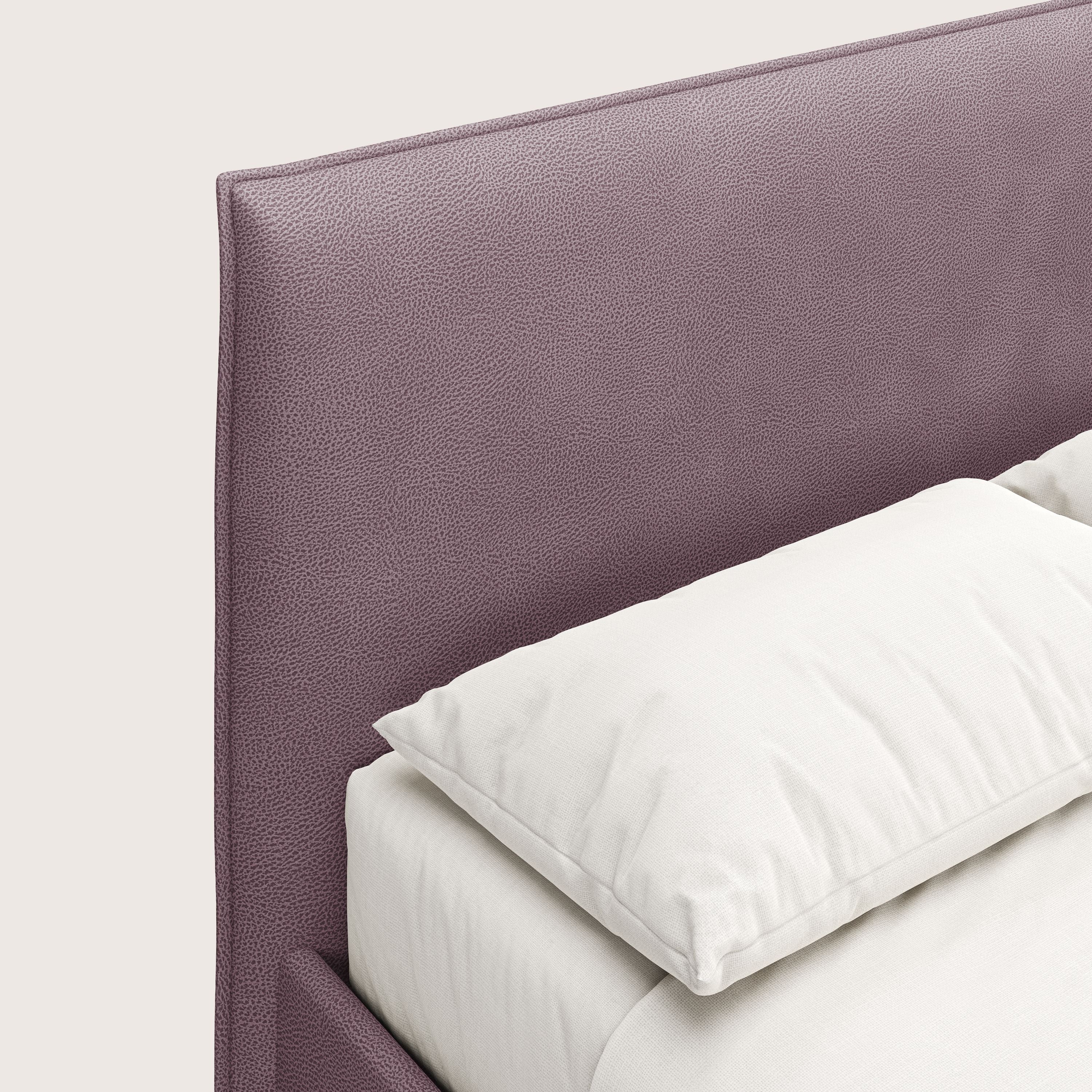 Primo piano del letto contenitore Nina di Letti.store, caratterizzato da un design minimale con rivestimento in microfibra rosa antimacchia effetto pelle e testata testurizzata, ordinatamente realizzata con biancheria da letto bianca su sfondo chiaro.