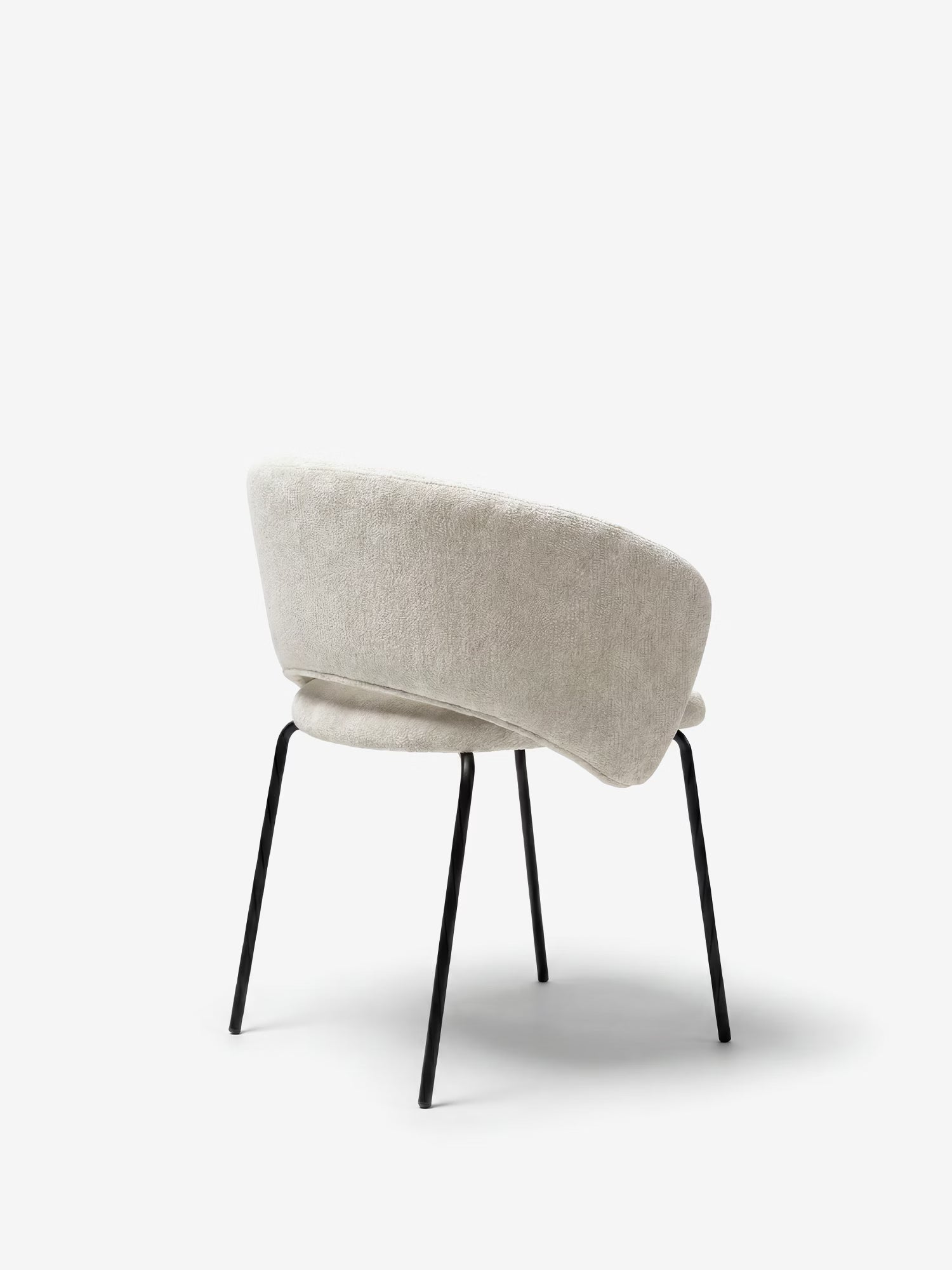 La sedia imbottita Fosca di Divani.Store presenta un design moderno con seduta e schienale arrotondati e imbottiti in tessuto beige chiaro certificato OEKO-TEX®, sottili gambe angolate in metallo nero e braccioli; nella foto è raffigurata vista da dietro su uno sfondo bianco.