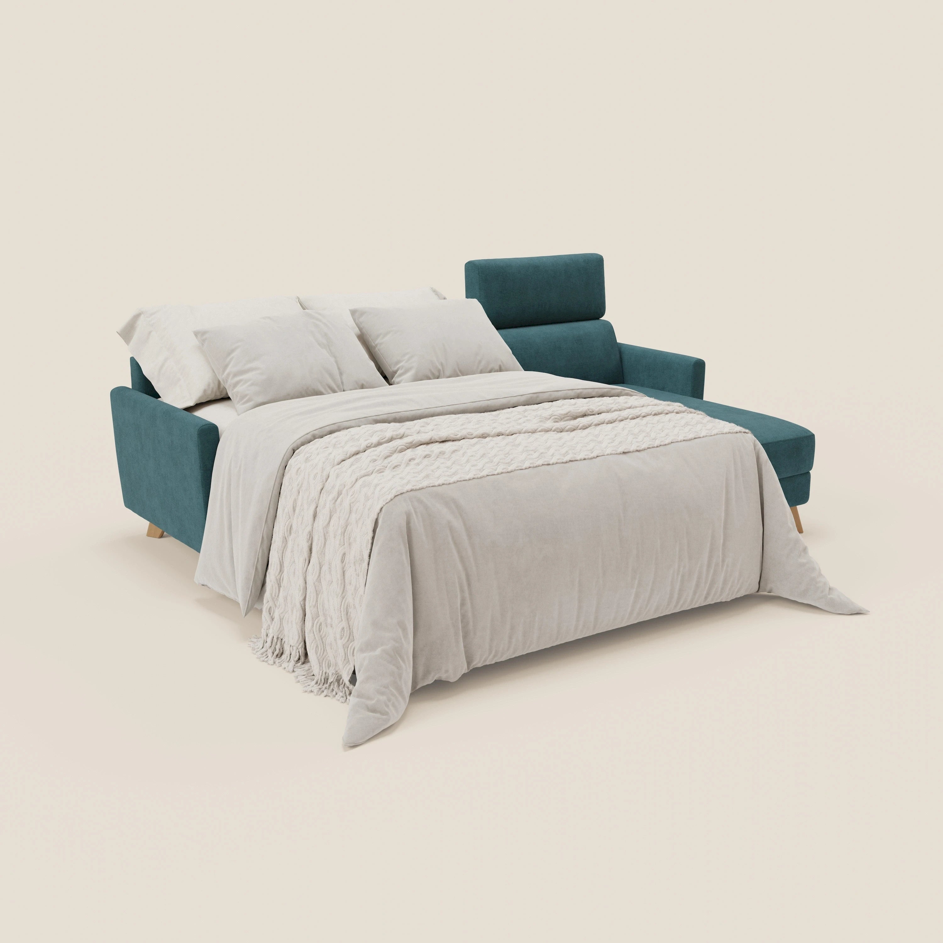 Il divano letto angolare sfoderabile Francy di Divani.Store in tessuto smacchiabile T17 petrolio è dotato di una chaise lounge con contenitore, di poggiatesta reclinabili e di biancheria da letto beige chiaro con tre cuscini su uno sfondo bianco sporco.