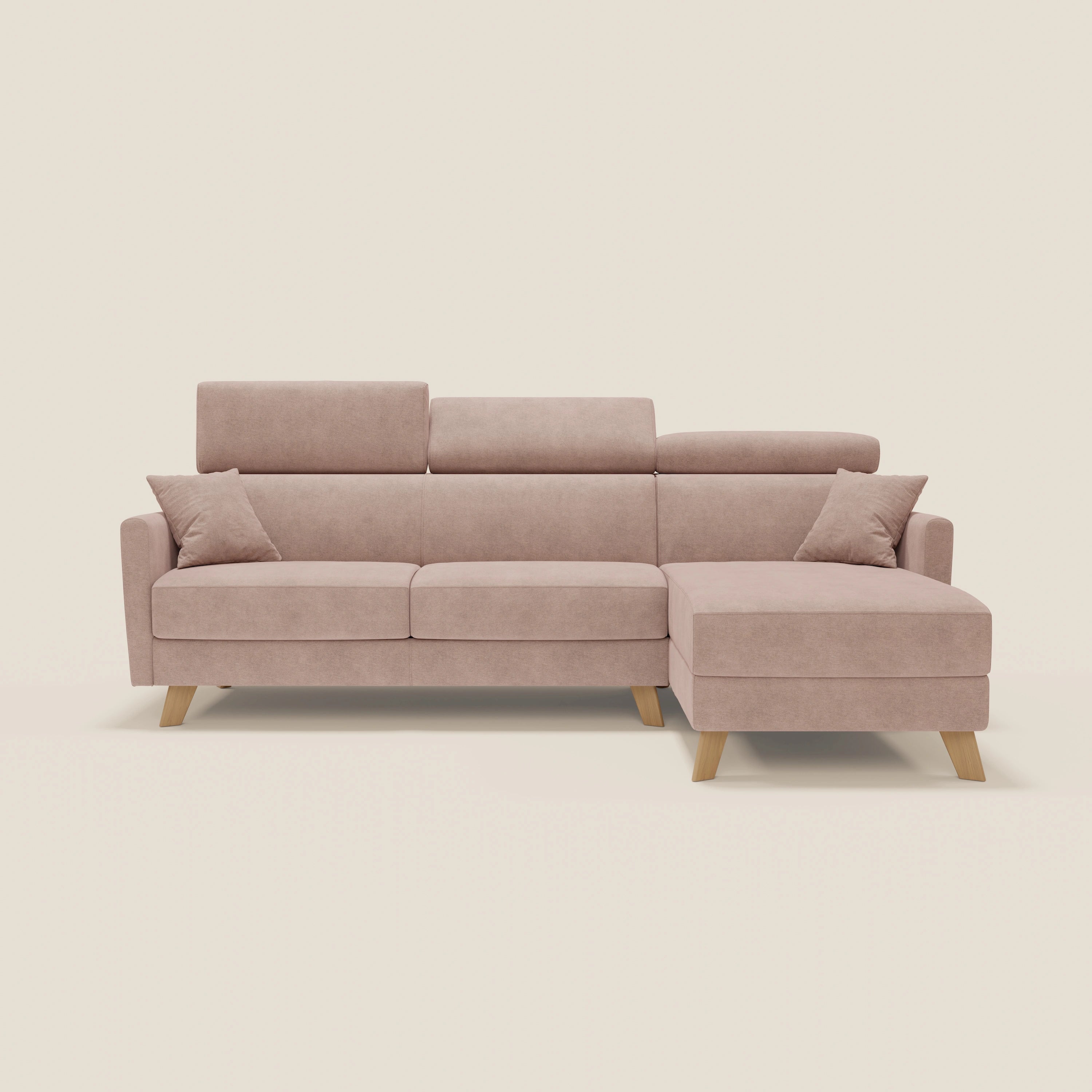 Il divano letto angolare Francy di Divani.Store è caratterizzato da un tessuto T17 antimacchia rosa blush, una chaise longue destra, due cuscini coordinati, gambe angolari in legno e poggiatesta regolabili, su uno sfondo bianco sporco.