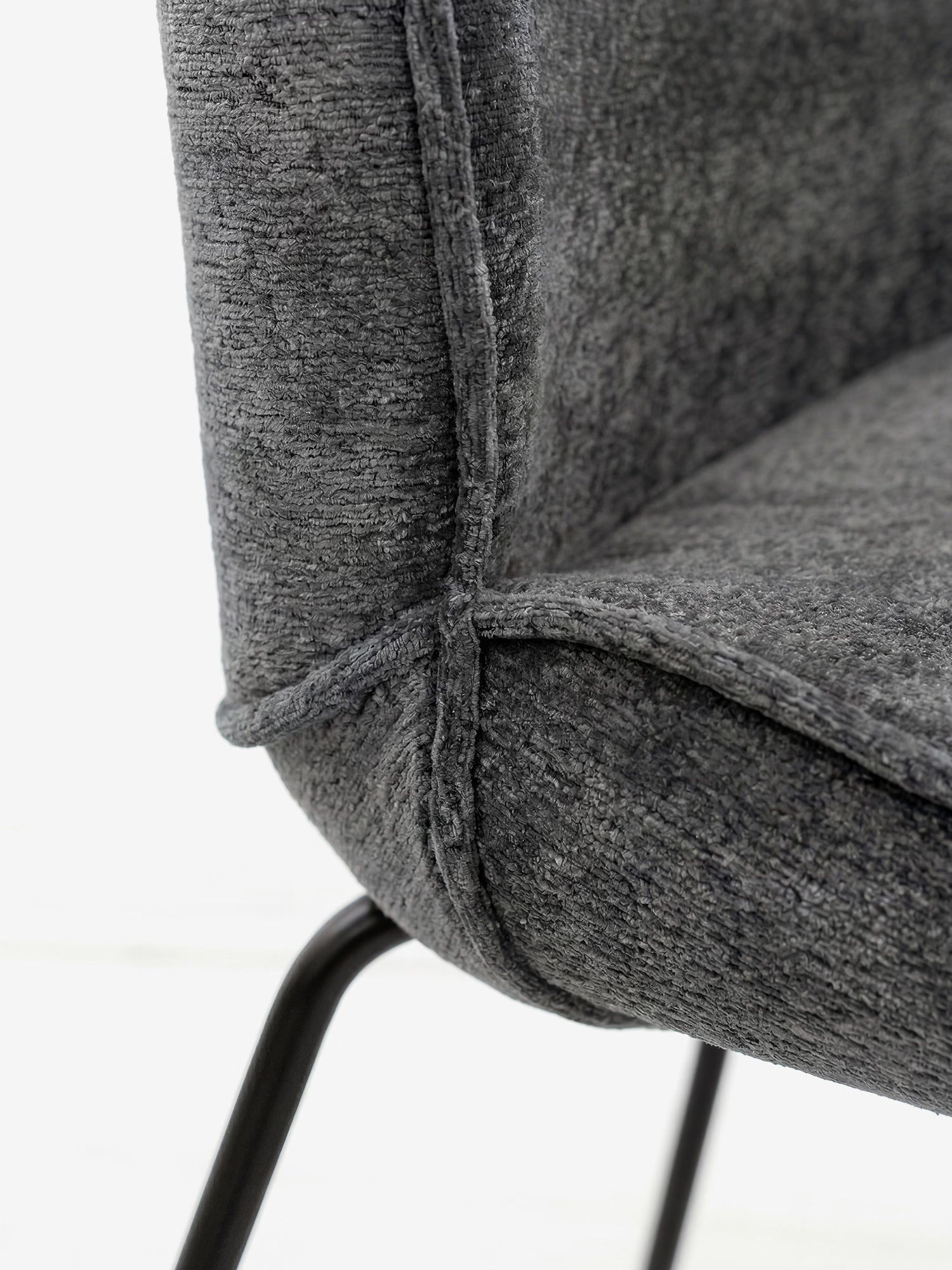 Primo piano della sedia imbottita Iride di Divani.Store, rivestita in morbido tessuto grigio scuro con trama in rilievo e cuciture a vista, caratterizzata da seduta e schienale imbottiti e dalla forma arrotondata, su gambe in metallo nero, su uno sfondo leggermente sfocato.