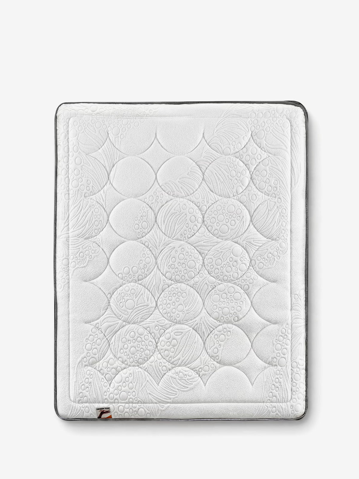 Un materasso KYROS quadrato e bianco di Divani.Store presenta un delicato motivo circolare in rilievo, impreziosito da sottili motivi a foglia. Progettato con molle a memoria di forma e molle insacchettate per un supporto posturale intelligente a 7 zone e il massimo comfort, questo lussuoso topper è bordato di grigio scuro lungo i bordi e presenta una piccola etichetta in tessuto marrone e bianco su un angolo inferiore. Lo sfondo rimane bianco a tinta unita.