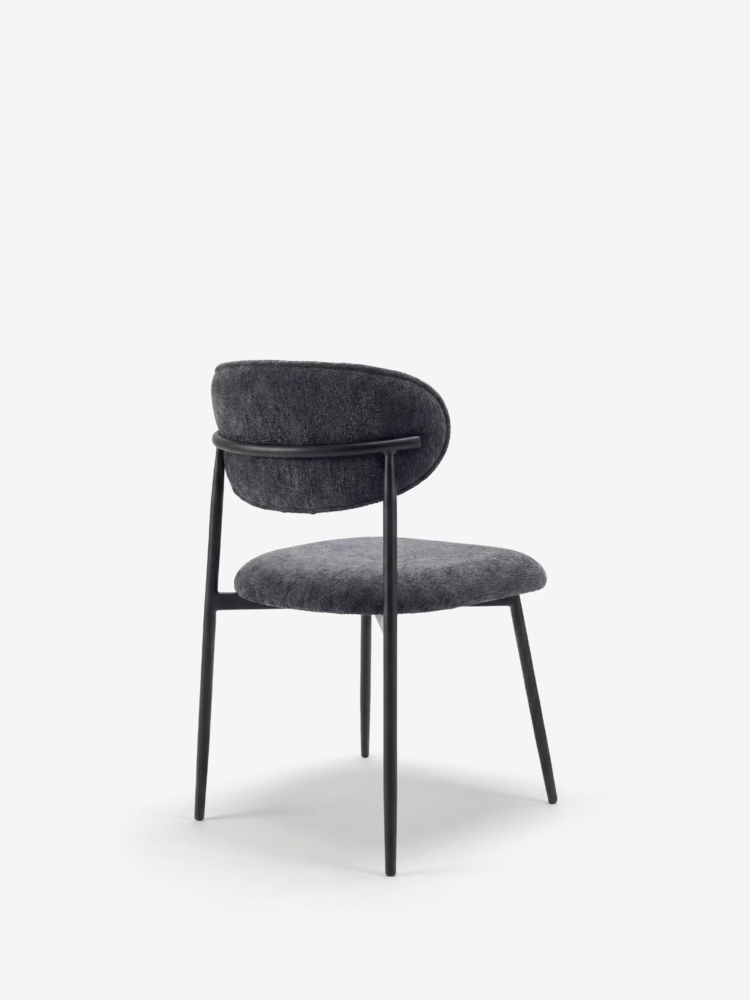 La Luce, una sedia imbottita in morbido tessuto ciniglia di Divani.Store, presenta uno schienale curvo e una seduta in tessuto grigio scuro, gambe sottili in metallo nero e un design minimalista; nella foto è ritratta di profilo su uno sfondo bianco.