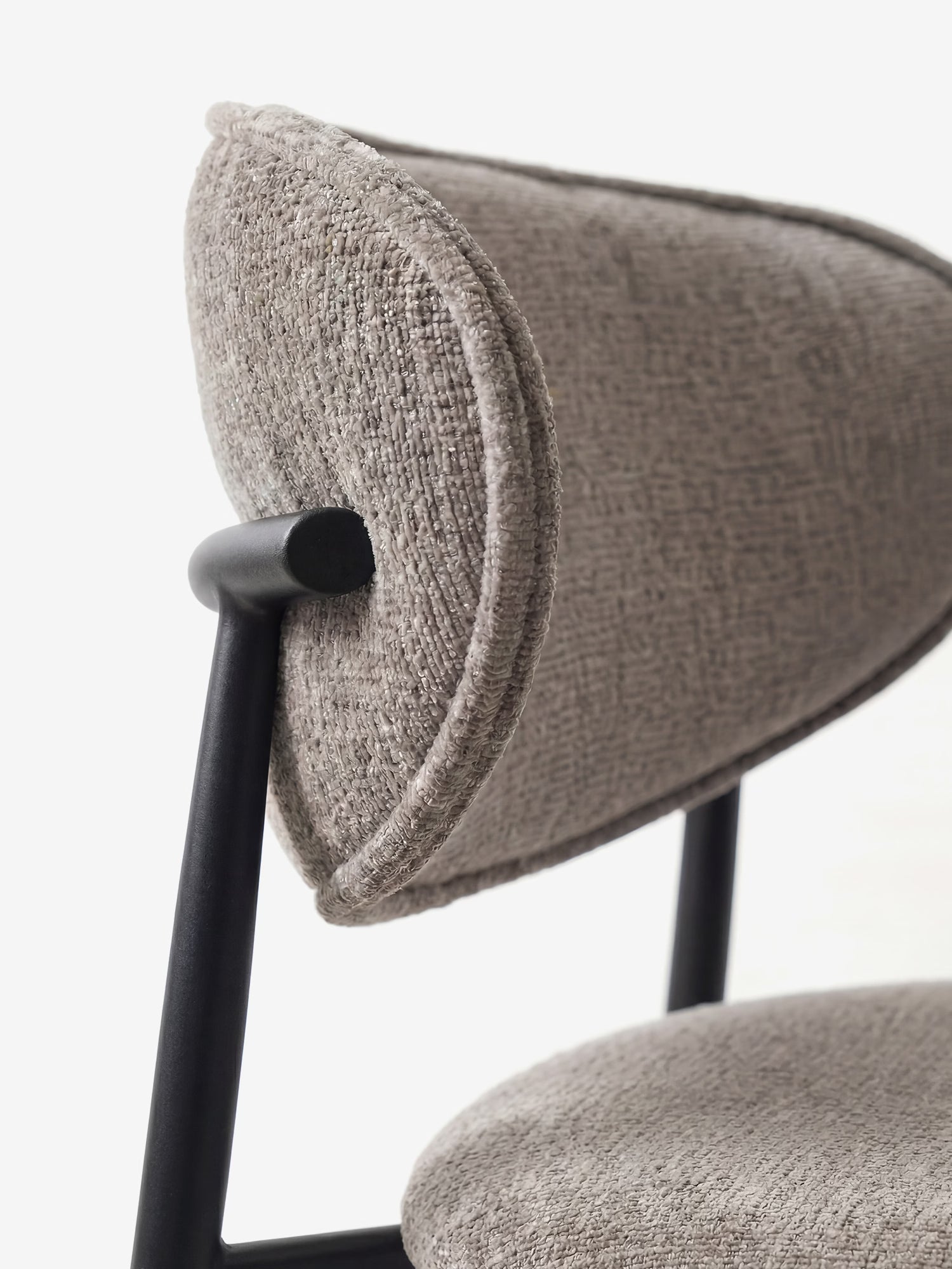 Primo piano della Luce Sedia, imbottita in morbido tessuto ciniglia di Divani.Store, caratterizzata da schienale e seduta grigio chiaro con trama in rilievo e design imbottito dalle linee curve, su un elegante telaio in metallo nero, su sfondo bianco.