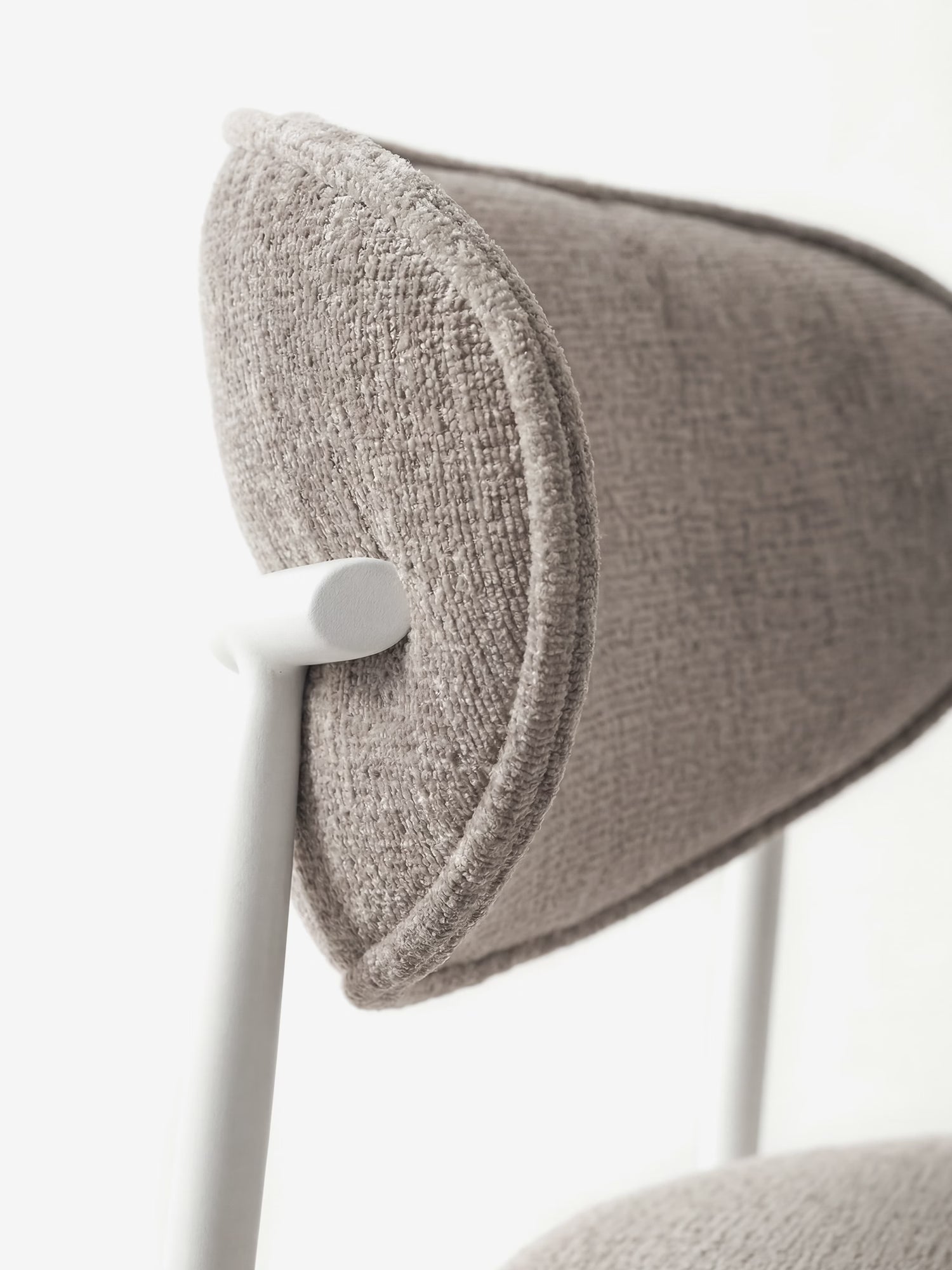 Primo piano della “Luce Sedia” di Divani.Store, una sedia imbottita con schienale curvo in tessuto, che ne mette in risalto il morbido rivestimento in ciniglia grigio chiaro e lo schienale arrotondato, sostenuto da una struttura minimalista in metallo bianco su uno sfondo luminoso.