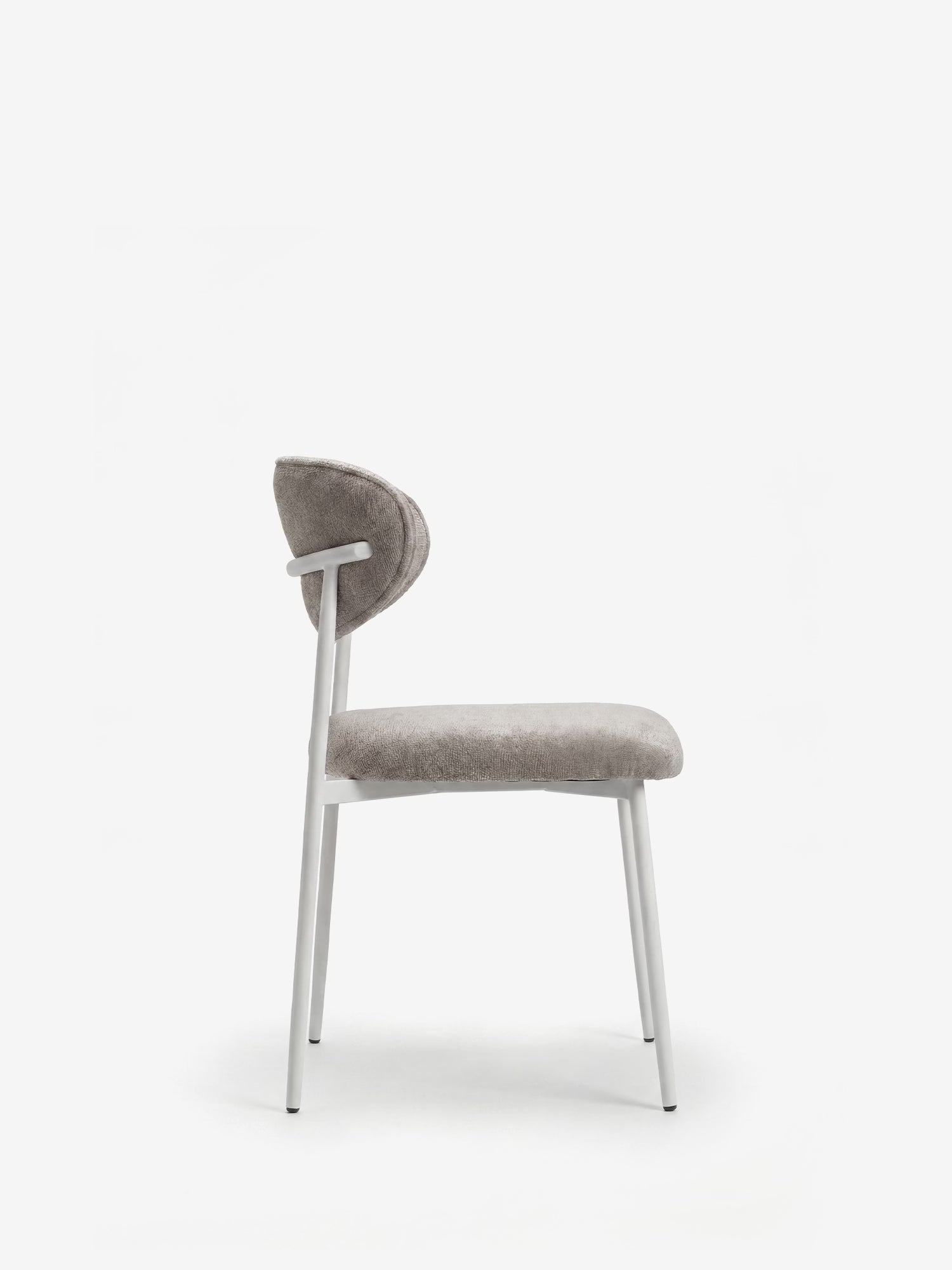 Vista laterale della sedia imbottita Luce con schienale curvo in tessuto di Divani.Store, caratterizzata da seduta e schienale rivestiti in grigio chiaro, con un elegante telaio e gambe in metallo bianco, in primo piano su uno sfondo bianco a tinta unita.