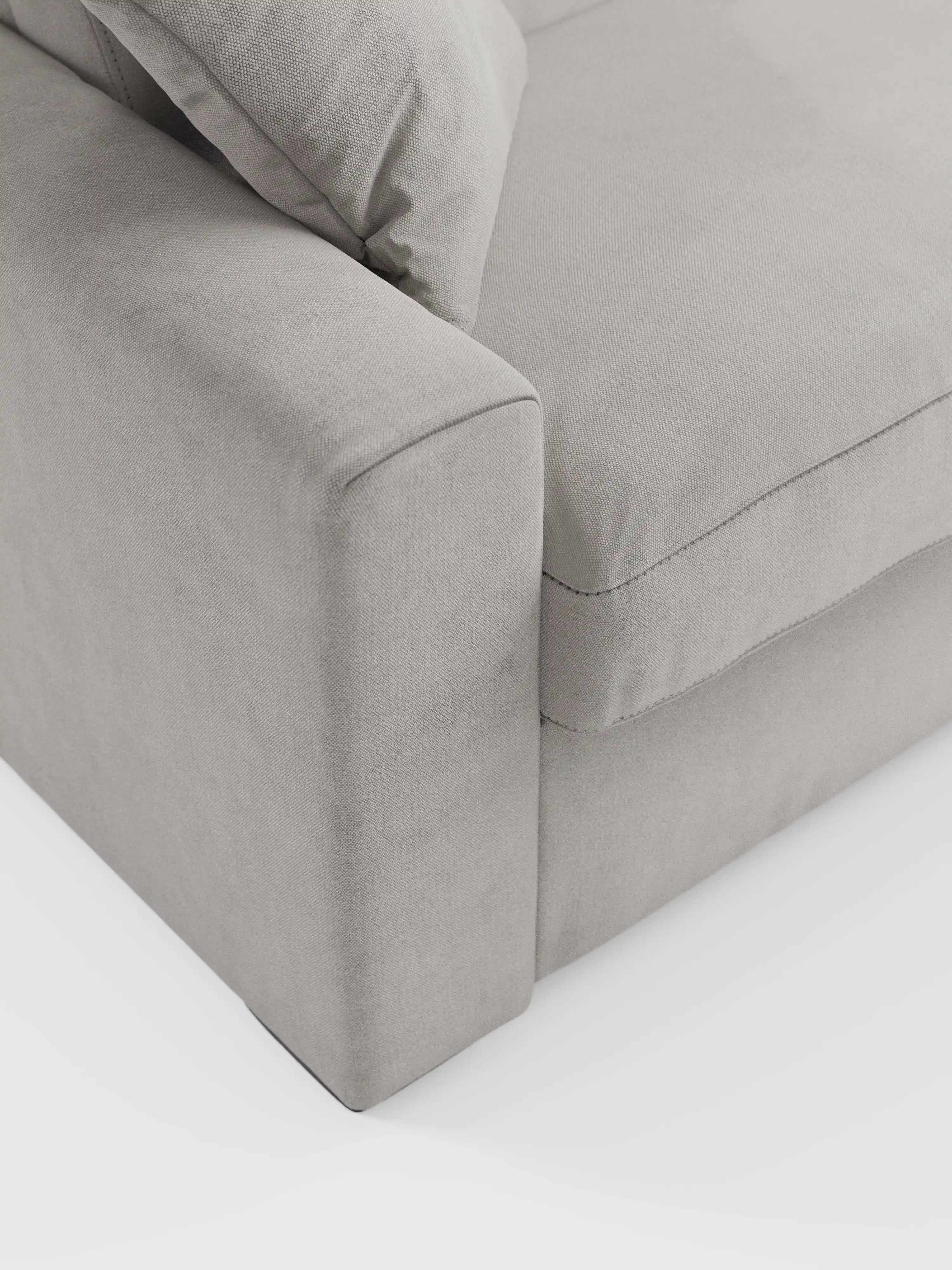 Primo piano del divano letto Maximus a 3 posti con materasso ALTO da 20 cm di Divani.Store, caratterizzato da braccioli spessi, un morbido cuscino di seduta e un cuscino dello schienale abbinato in tessuto grigio chiaro Oeko-Tex resistente alle macchie. Su uno sfondo bianco, le sue linee pulite e la possibilità di scegliere poggiatesta reclinabili mettono in risalto il design minimalista e contemporaneo del divano.