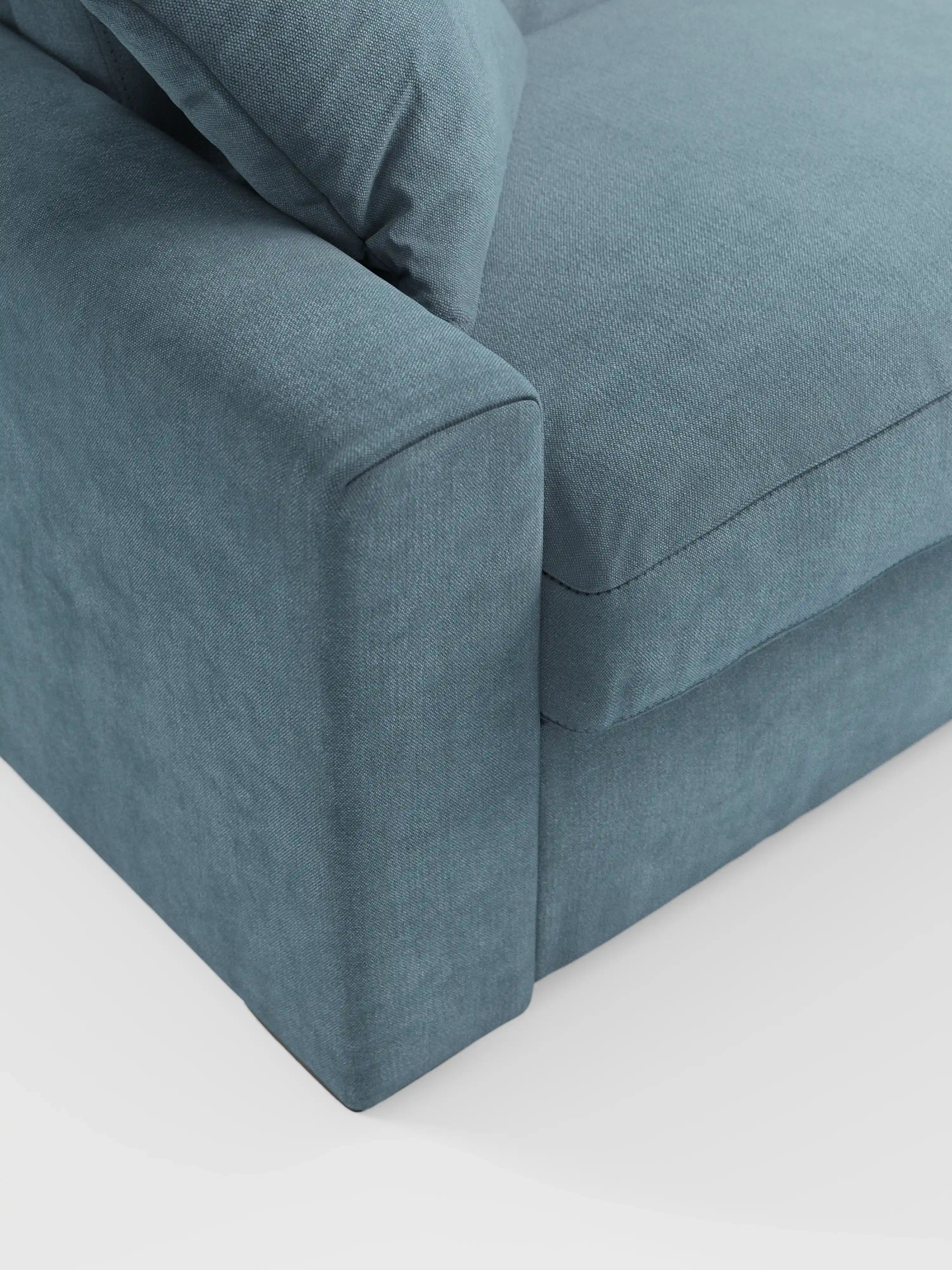 Primo piano del divano letto a tre posti Maximus con materasso ALTO da 20 cm di Divani.Store, rivestito in tessuto Oeko-Tex blu-grigio testurizzato e resistente alle macchie. L'immagine mette in risalto il bracciolo, il cuscino della seduta e parte del cuscino dello schienale — tutti caratterizzati da linee pulite e uno stile contemporaneo — esaltando l'eleganza di questo divano letto a tre posti con poggiatesta regolabili. Lo sfondo è una superficie liscia e di colore chiaro.