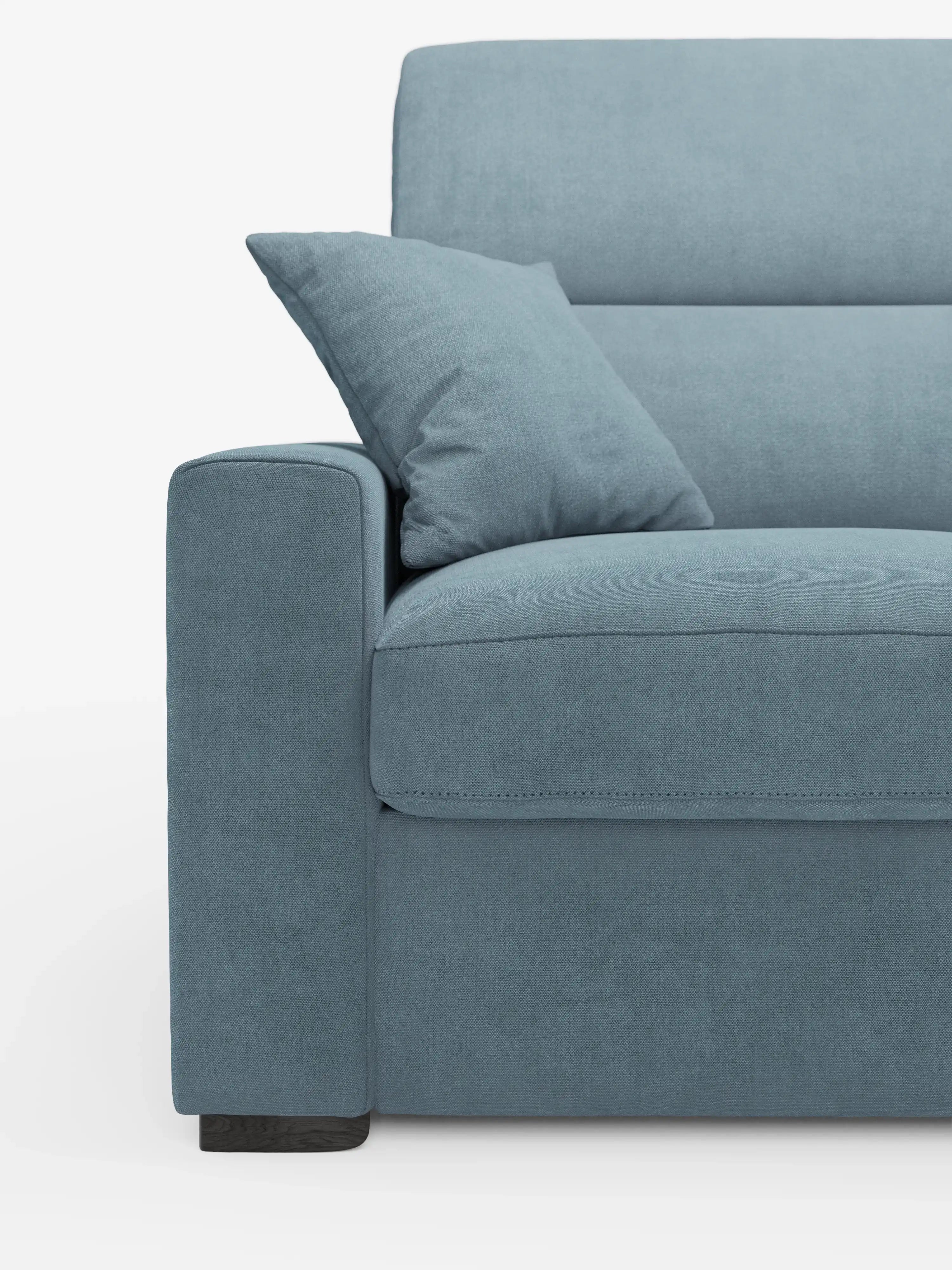 Un primo piano del moderno divano letto Maximus a 3 posti con rivestimento blu e materasso ALTO 20 cm di Divani.Store, caratterizzato da un unico cuscino coordinato sulla seduta. L'immagine mostra il lato sinistro, mettendo in risalto il bracciolo, la seduta, lo schienale con poggiatesta reclinabili in tessuto antimacchia Oeko-Tex e la gamba corta in legno scuro. Lo sfondo è bianco a tinta unita.