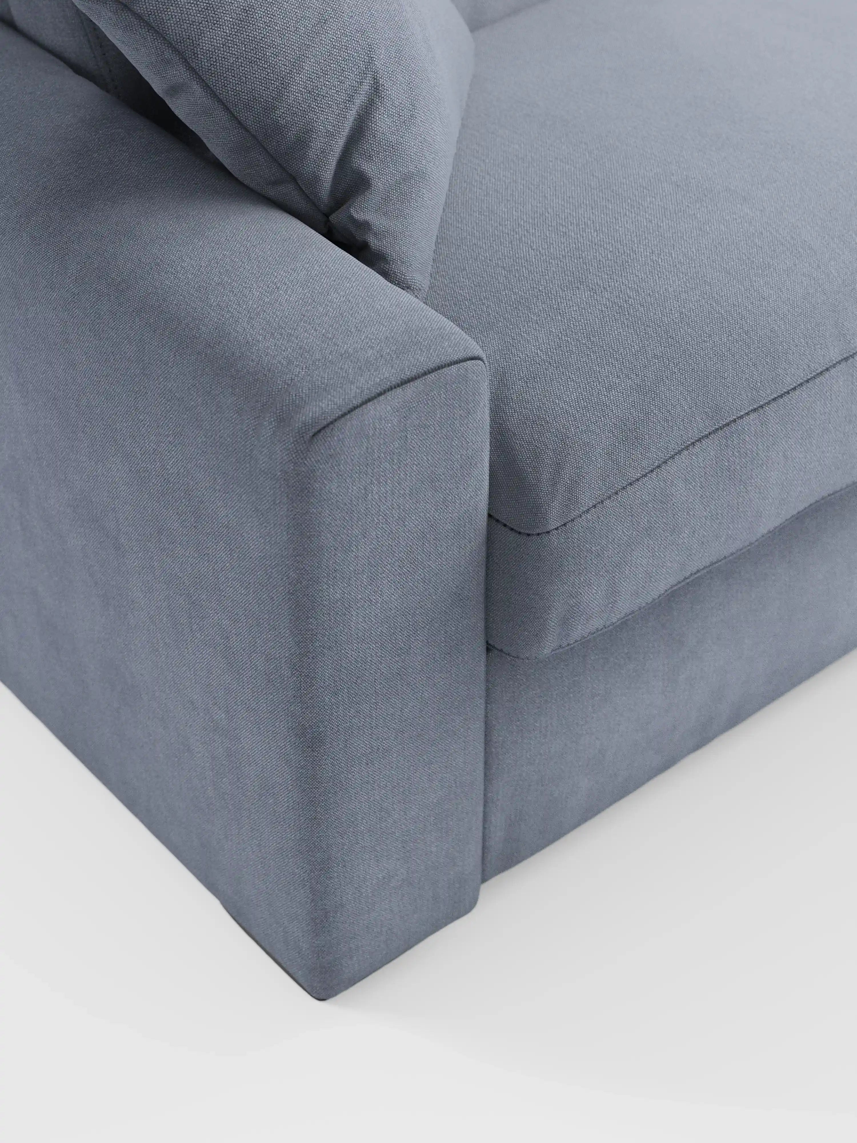 Primo piano del divano letto Maximus a 3 posti con materasso ALTO da 20 cm di Divani.Store, rivestito in morbido tessuto smacchiabile Oeko-Tex di colore grigio medio. L’immagine mette in risalto i morbidi cuscini della seduta e dello schienale, un ampio bracciolo imbottito con poggiatesta reclinabili e linee pulite e semplici. Sullo sfondo bianco, spicca il design minimalista del divano.