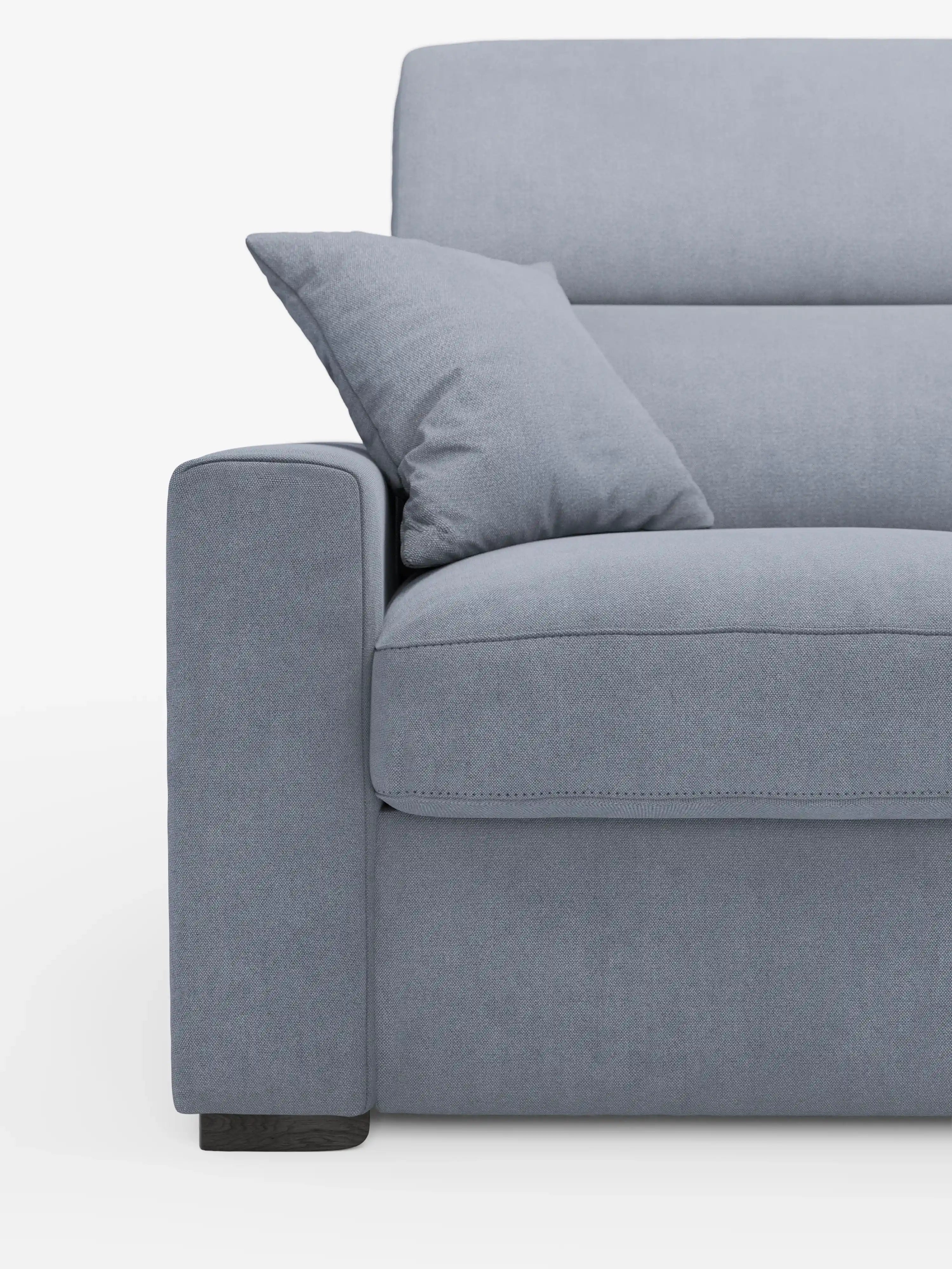 Primo piano del lato sinistro del divano letto a 3 posti Maximus con materasso ALTO da 20 cm di Divani.Store, realizzato in tessuto azzurro resistente alle macchie certificato Oeko-Tex, con cuscino quadrato abbinato, bracciolo, cuscino di seduta e parte dello schienale con poggiatesta regolabili; il tutto su uno sfondo bianco a tinta unita.