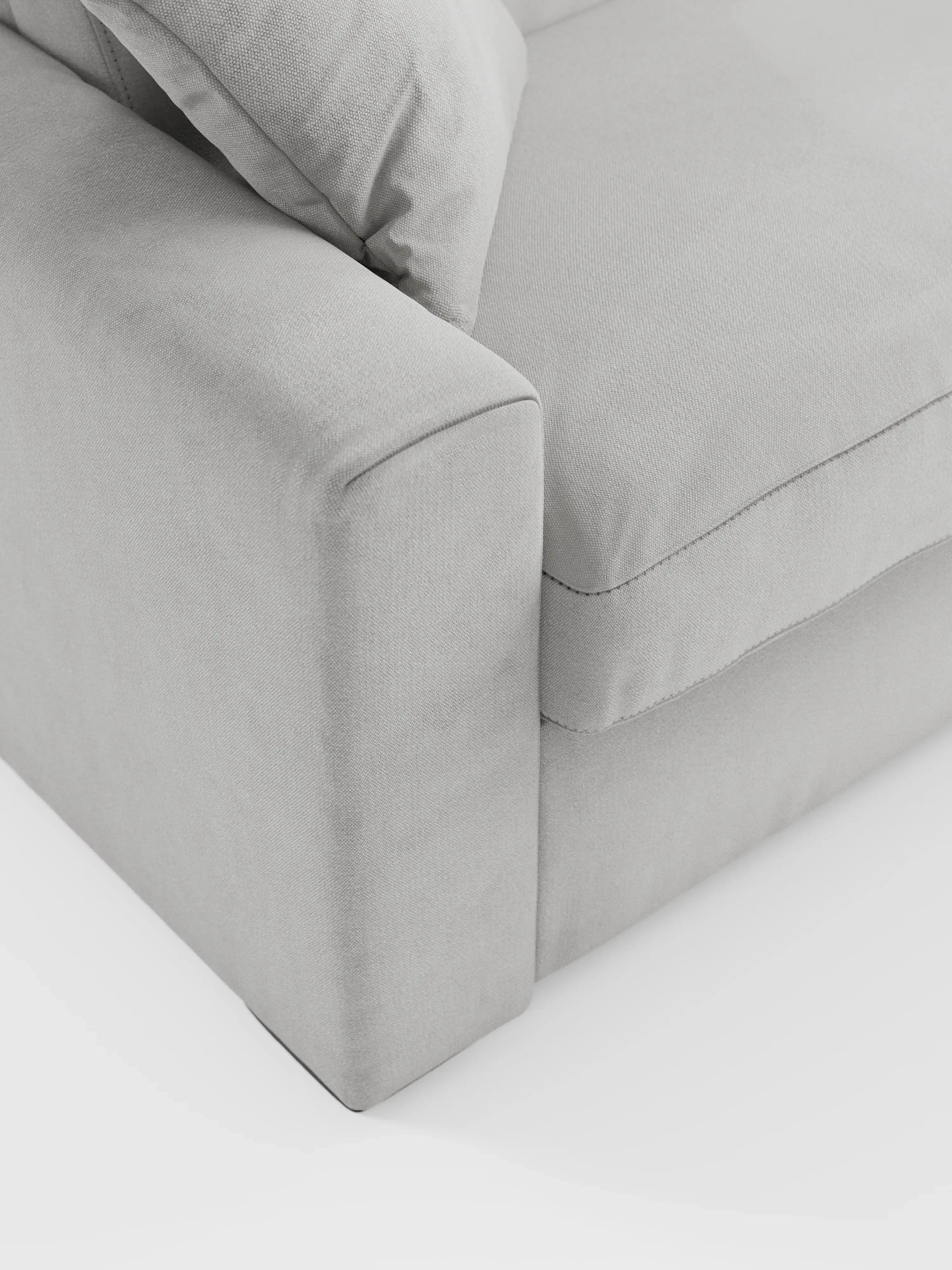 Primo piano dell'angolo del divano letto a 3 posti Maximus con materasso ALTO da 20 cm di Divani.Store, con bracciolo, cuscino di seduta e cuscino dello schienale realizzati in un moderno tessuto grigio chiaro Oeko-Tex antimacchia, caratterizzato da linee morbide e pulite e da cuciture minimaliste — raffigurato su sfondo bianco.
