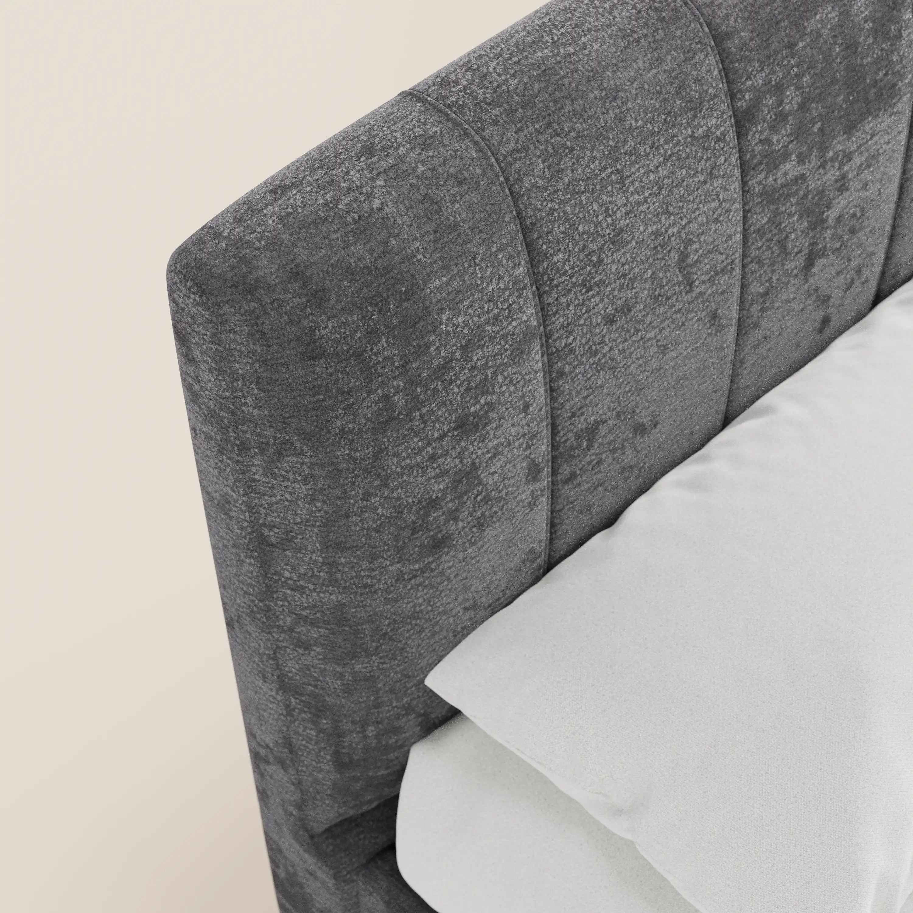 Vista dall'alto obliqua del letto imbottito con contenitore ONYX di Letti.store, caratterizzato da una testiera alta in tessuto grigio scuro certificato Oeko-Tex® con cuciture verticali, con cuscino e biancheria da letto bianchi su uno sfondo neutro.
