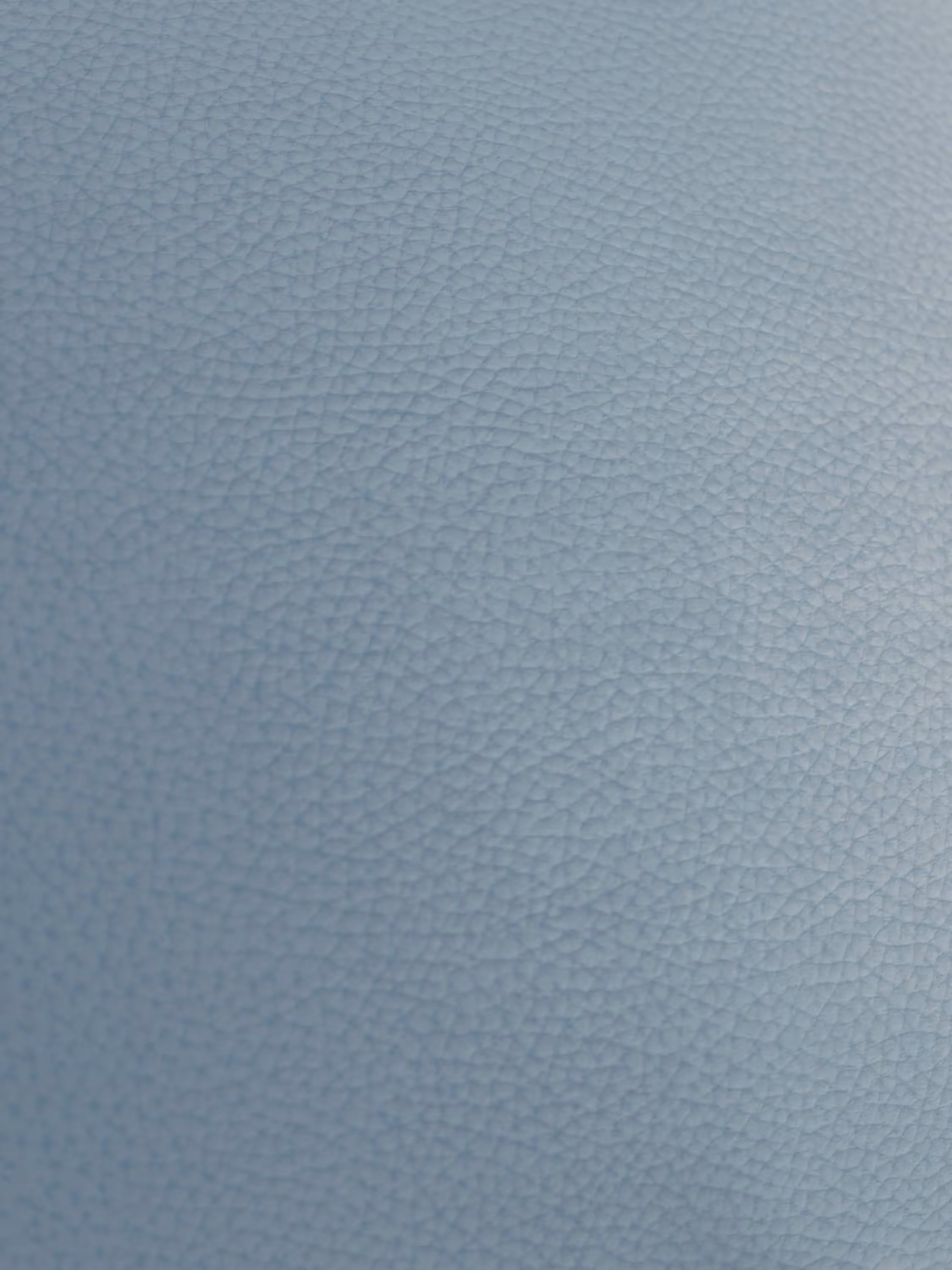 Primo piano della poltrona Chester di Divani.Store, realizzata in pelle vera di elevato spessore. La superficie azzurra presenta una distribuzione uniforme di sottili venature simili a ciottoli — caratteristiche della vera pelle — e si distingue per una finitura leggermente lucida che mette in risalto la lavorazione artigianale capitonné.