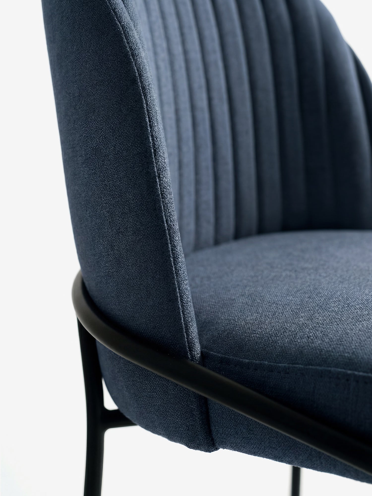 Primo piano della sedia imbottita "Plissè" in tessuto impermeabile di Divani.Store, con schienale plissettato, seduta imbottita liscia ed eleganti gambe in metallo nero. Immagine scattata su uno sfondo bianco a tinta unita.