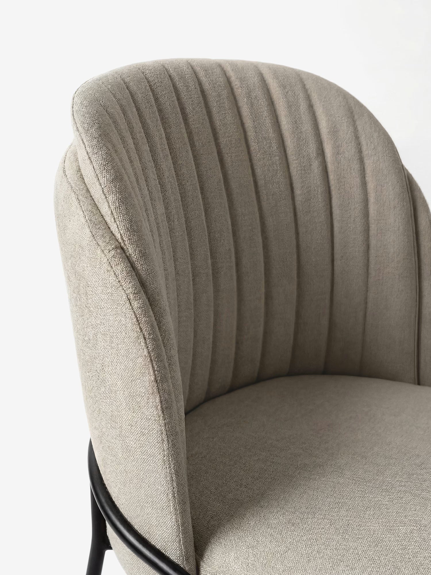 Un primo piano della sedia imbottita Plissè in tessuto impermeabile di Divani.Store, caratterizzata da uno schienale alto e ricurvo con cuciture plissettate e braccioli arrotondati, impreziosita da eleganti gambe in metallo nero che le conferiscono un tocco di eleganza contemporanea.